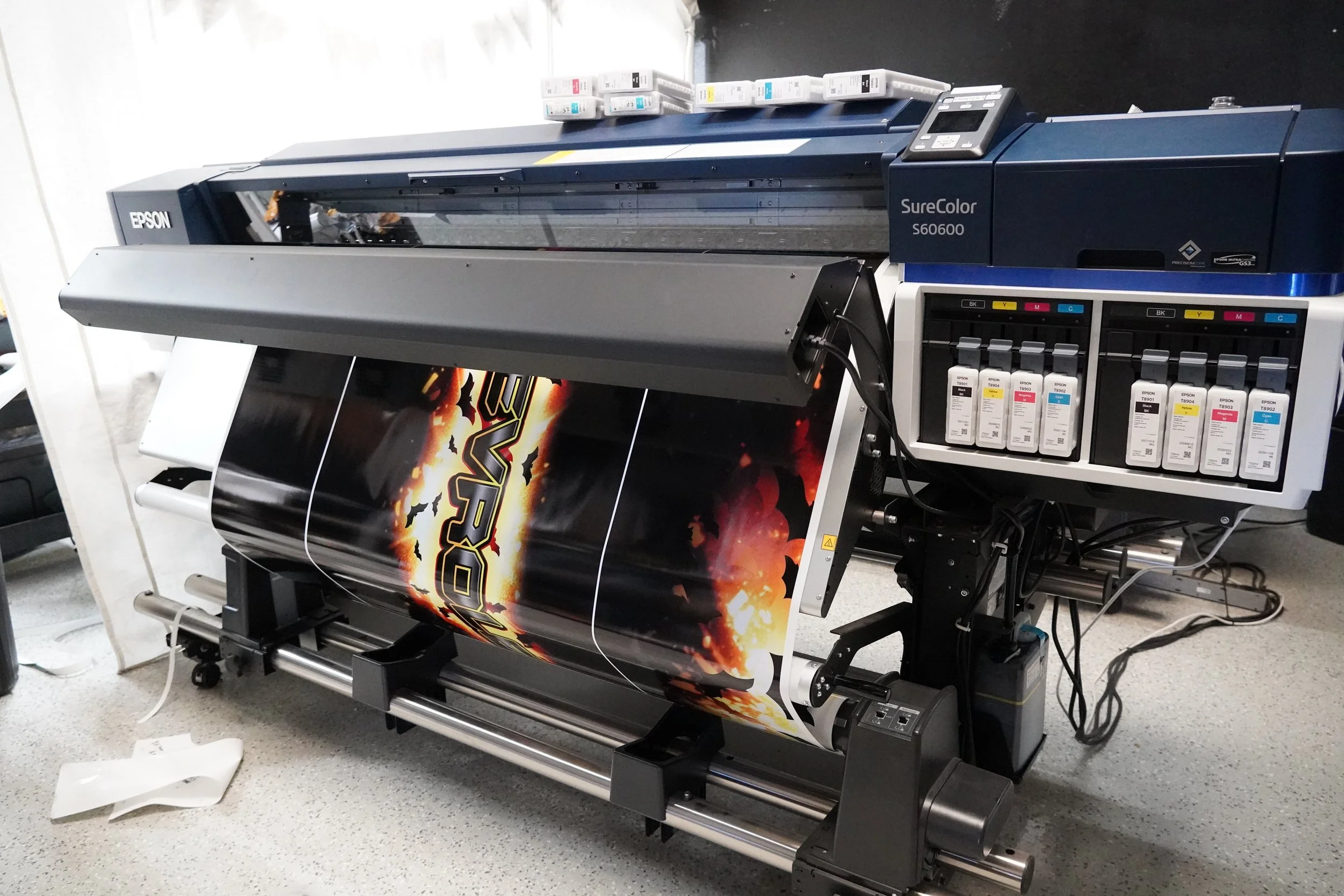 A large Epson SureColor S60600 large format printer printing a vibrant graphic with fiery colors and a black background.