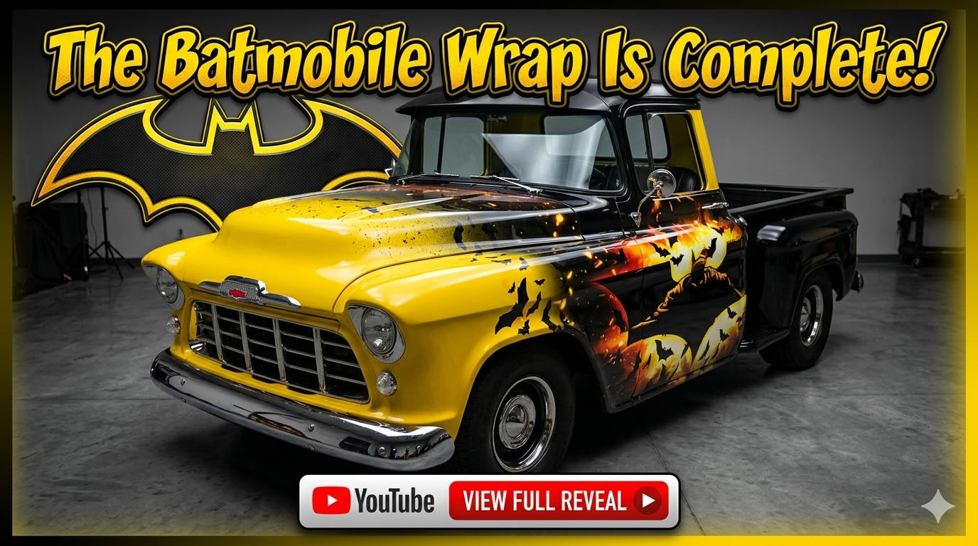 A vintage Chevrolet truck with Batman-themed custom artwork, featuring a large bat symbol on the hood and Batman silhouette with bats on the sides, parked indoors with a Batman logo backdrop.