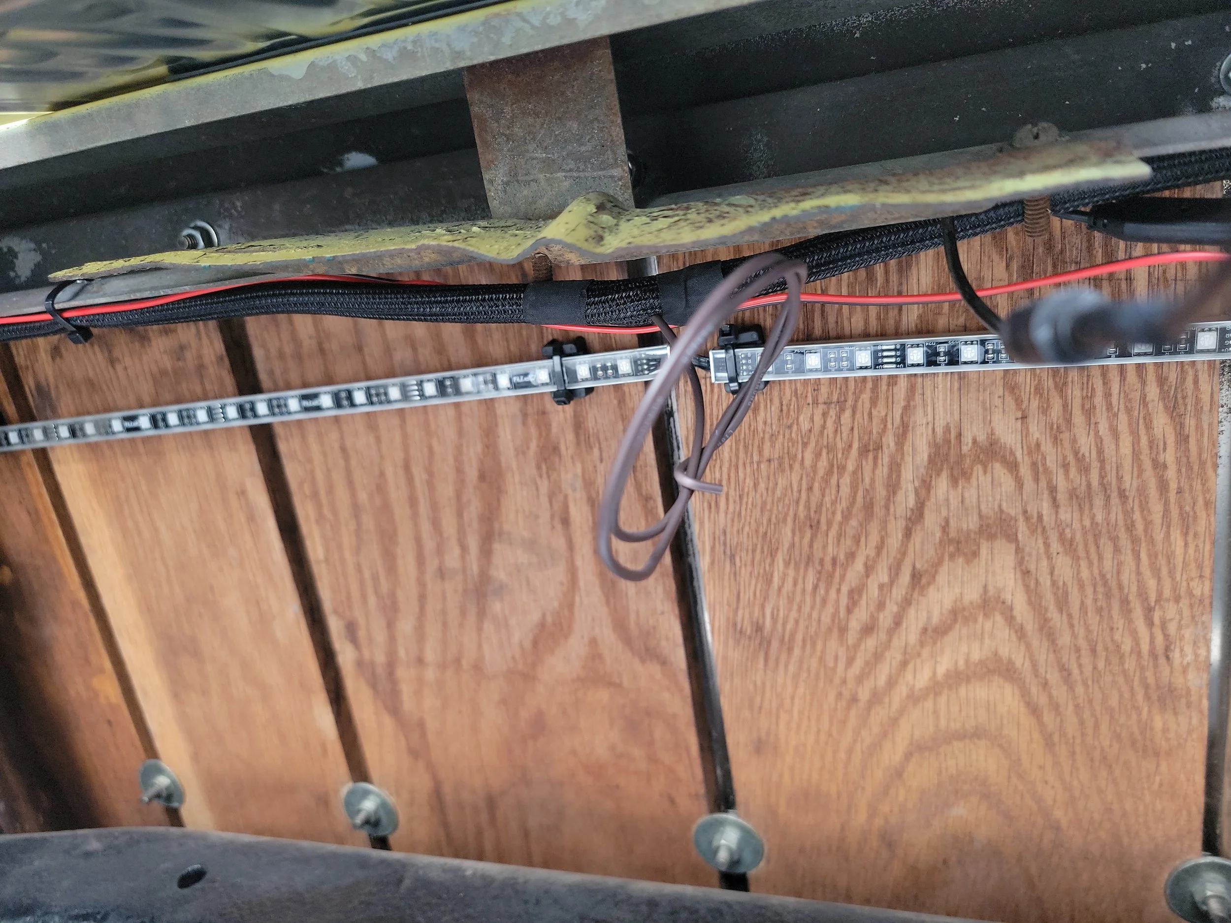 Viewing underneath a table or bench showing the wood floor, some cables, and metal bolts.