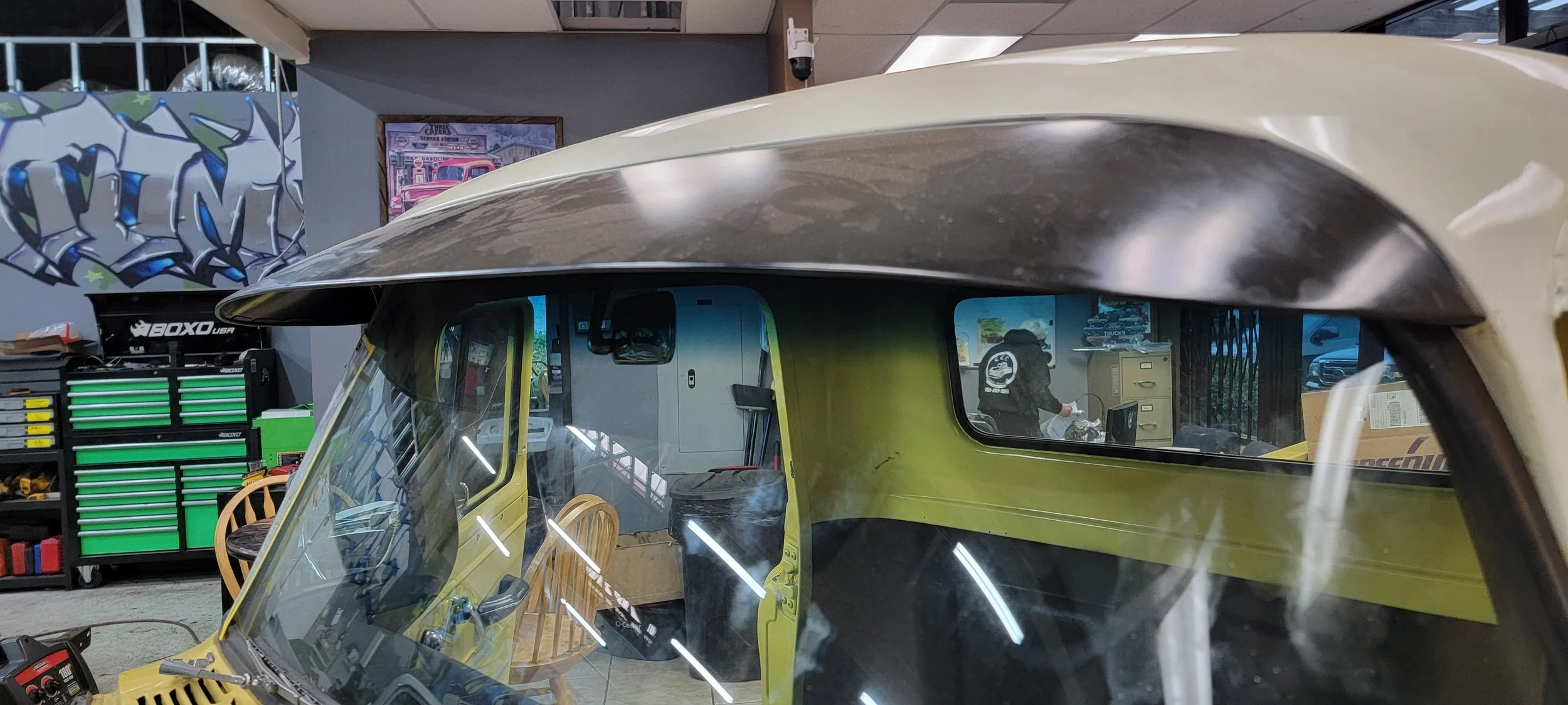 A vintage yellow vehicle with a large black roof parked inside a garage or workshop, surrounded by various tools and equipment.