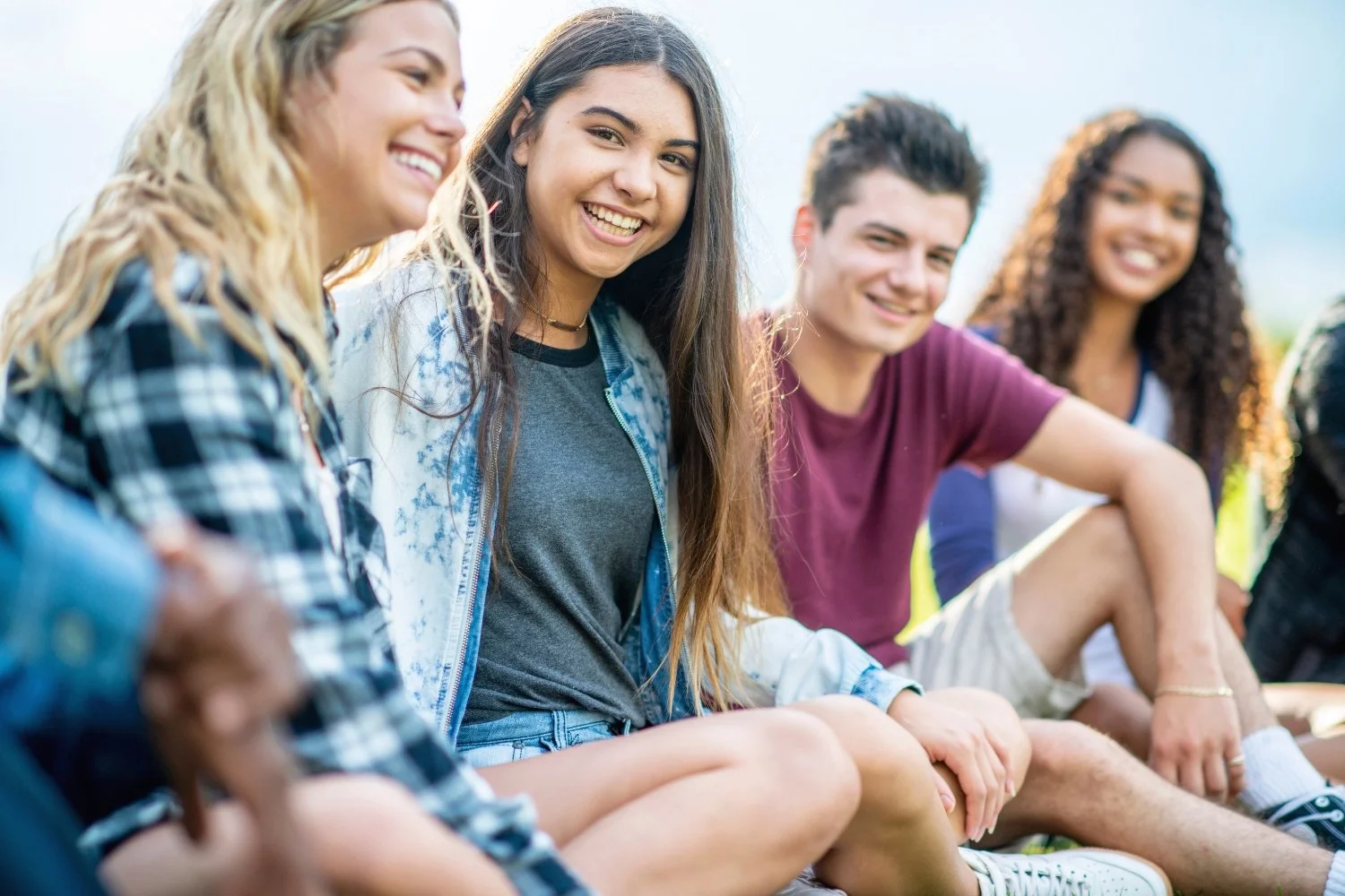 A group of five young people sitting outdoors, smiling and enjoying each other's company.