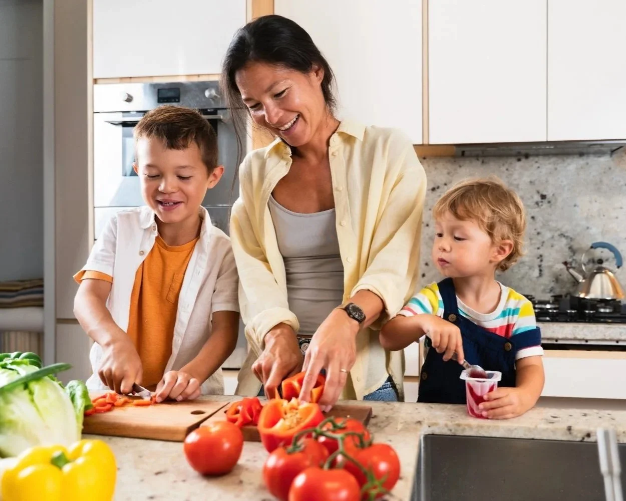 A woman and two young boys in a kitchen cutting vegetables and preparing food.