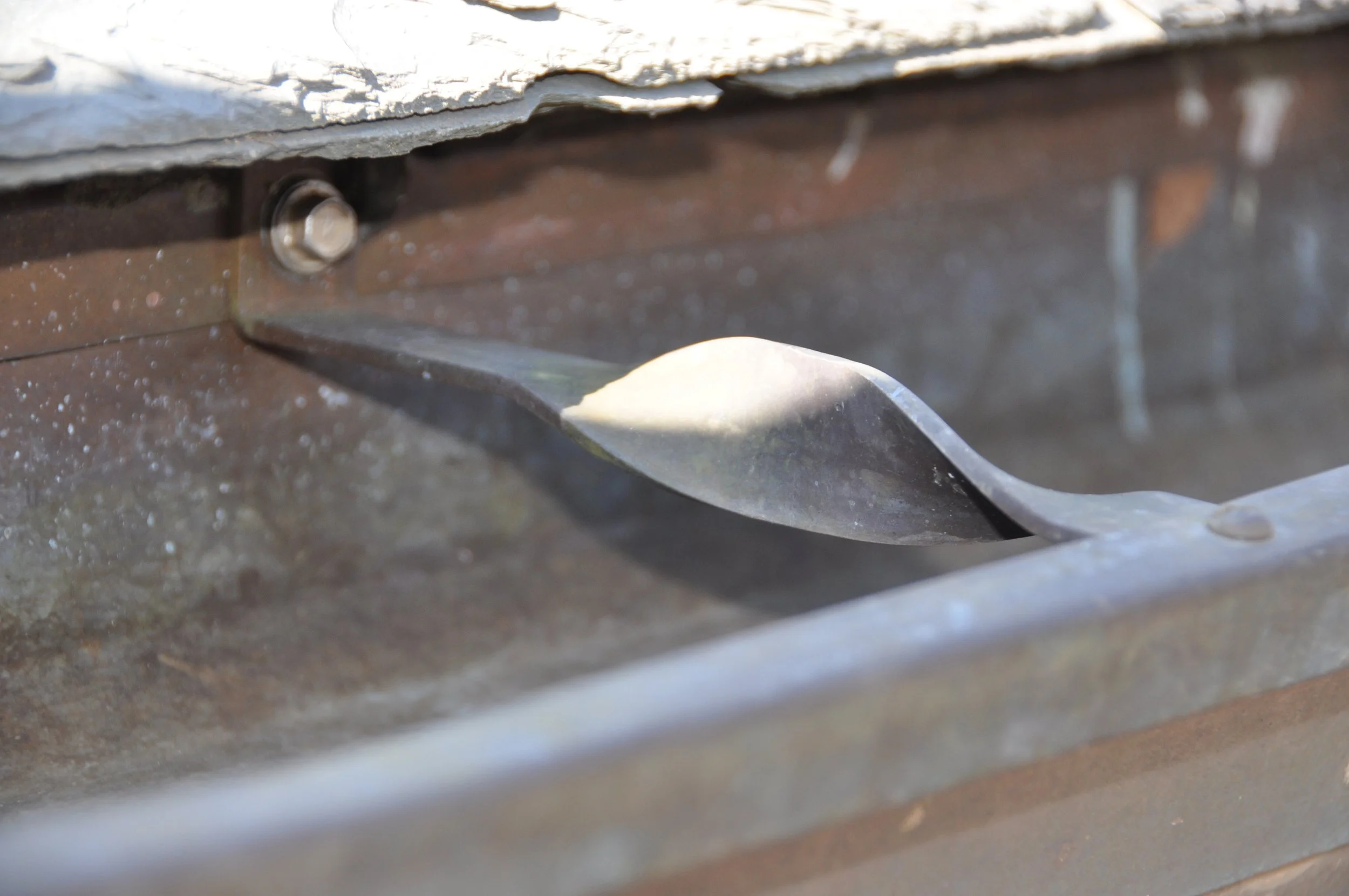 Close-up of a metal window or vent with a latch and rusted screws.