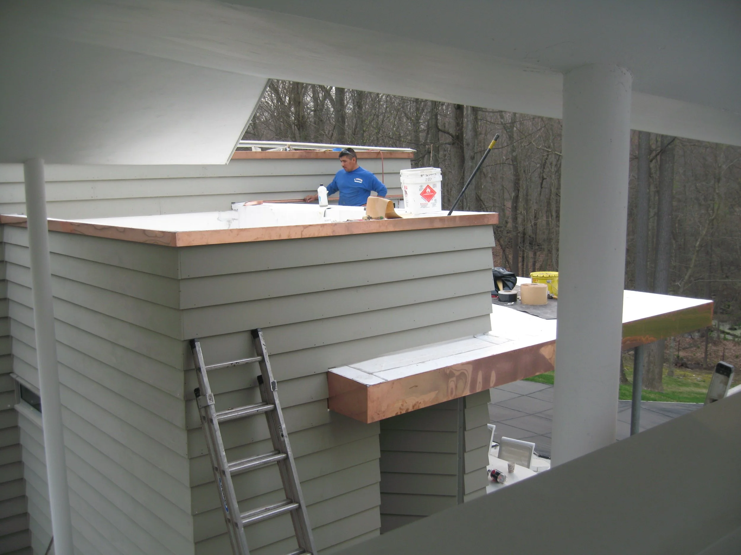 Man working on a construction project on the roof of a house, surrounded by construction materials and tools.