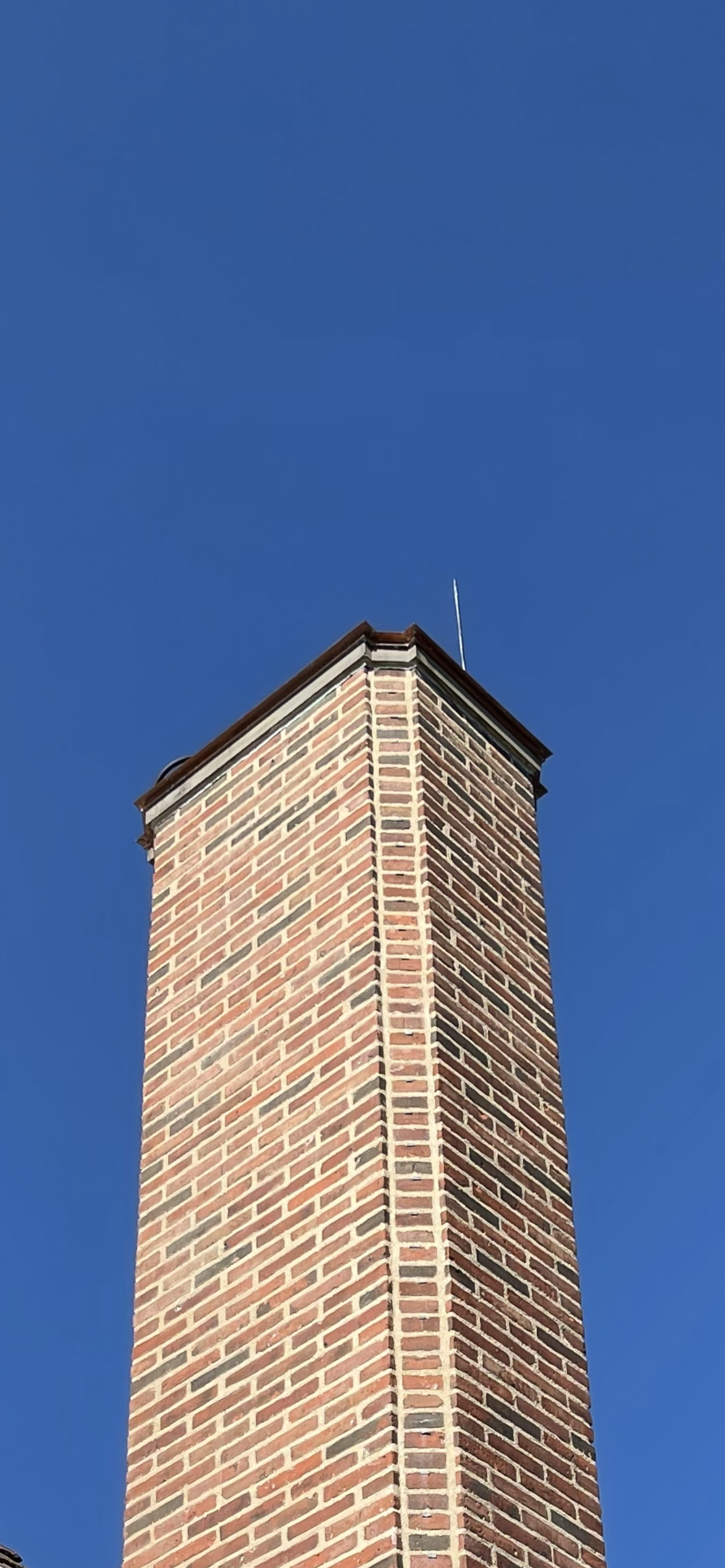 Close-up of a brick chimney against a clear blue sky.