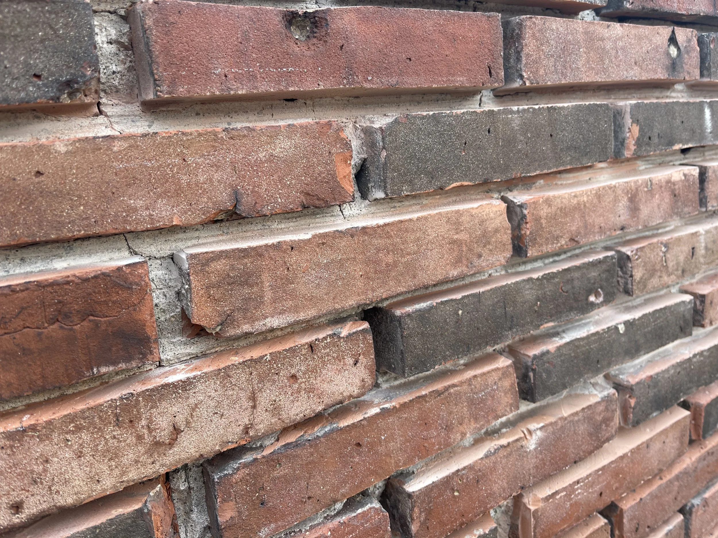 Close-up view of a brick wall with red and gray bricks, showing some imperfections and mortar joints.
