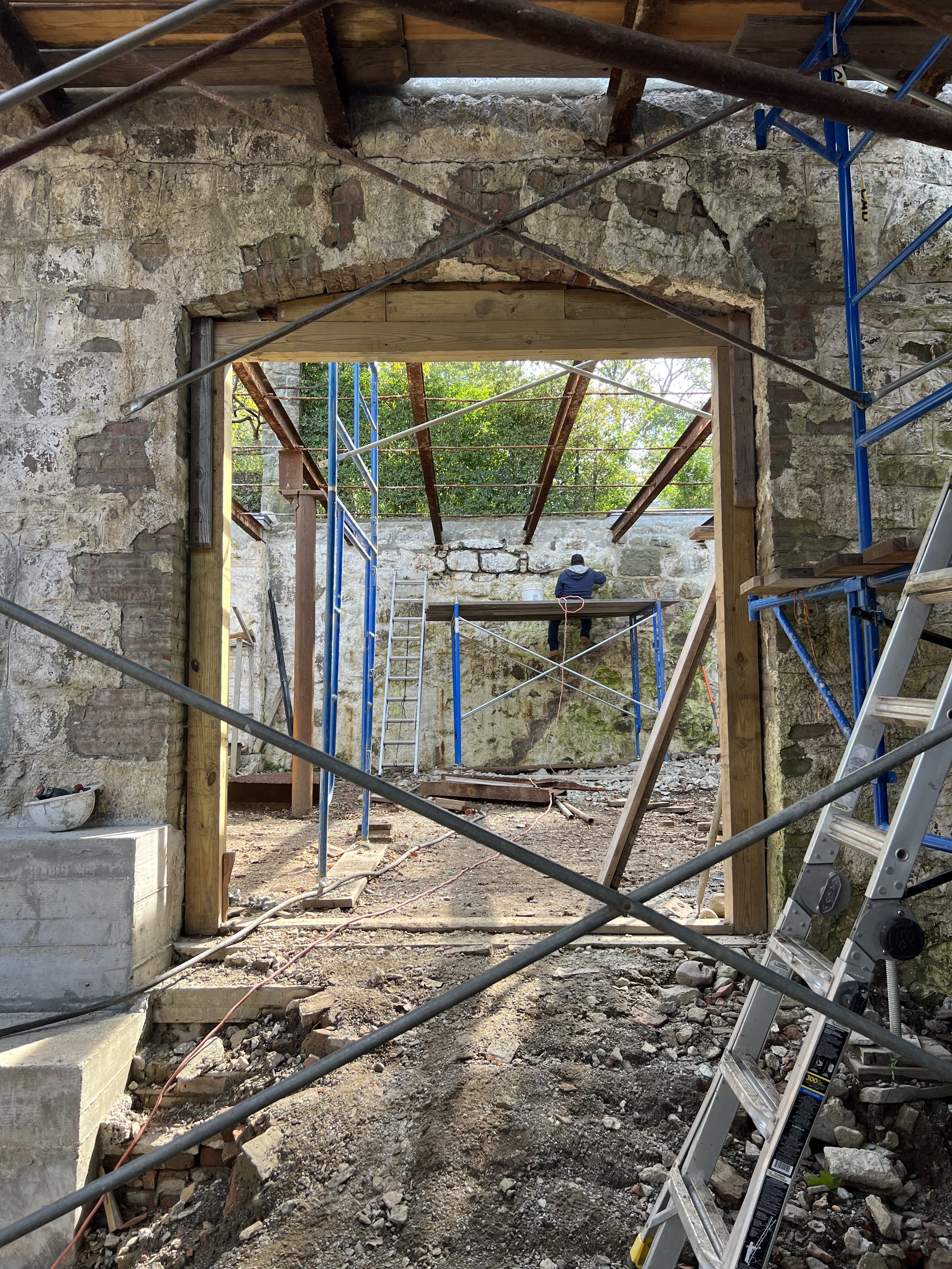 Construction site inside a building undergoing renovation with exposed brick and stone walls, scaffolding, and a worker in the background.