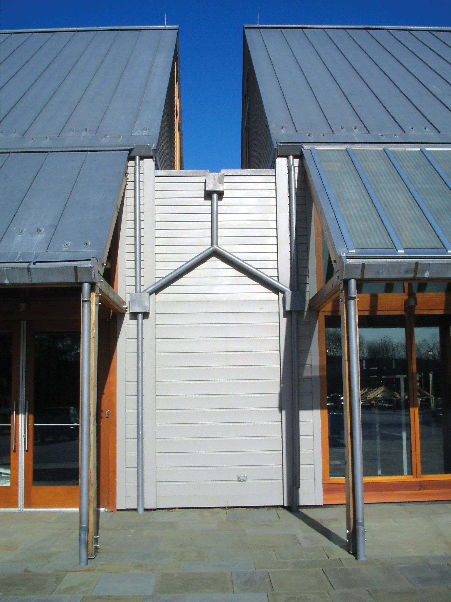Modern building with tall metal roofs, white siding, large glass windows, and orange frame accents, under a clear blue sky.