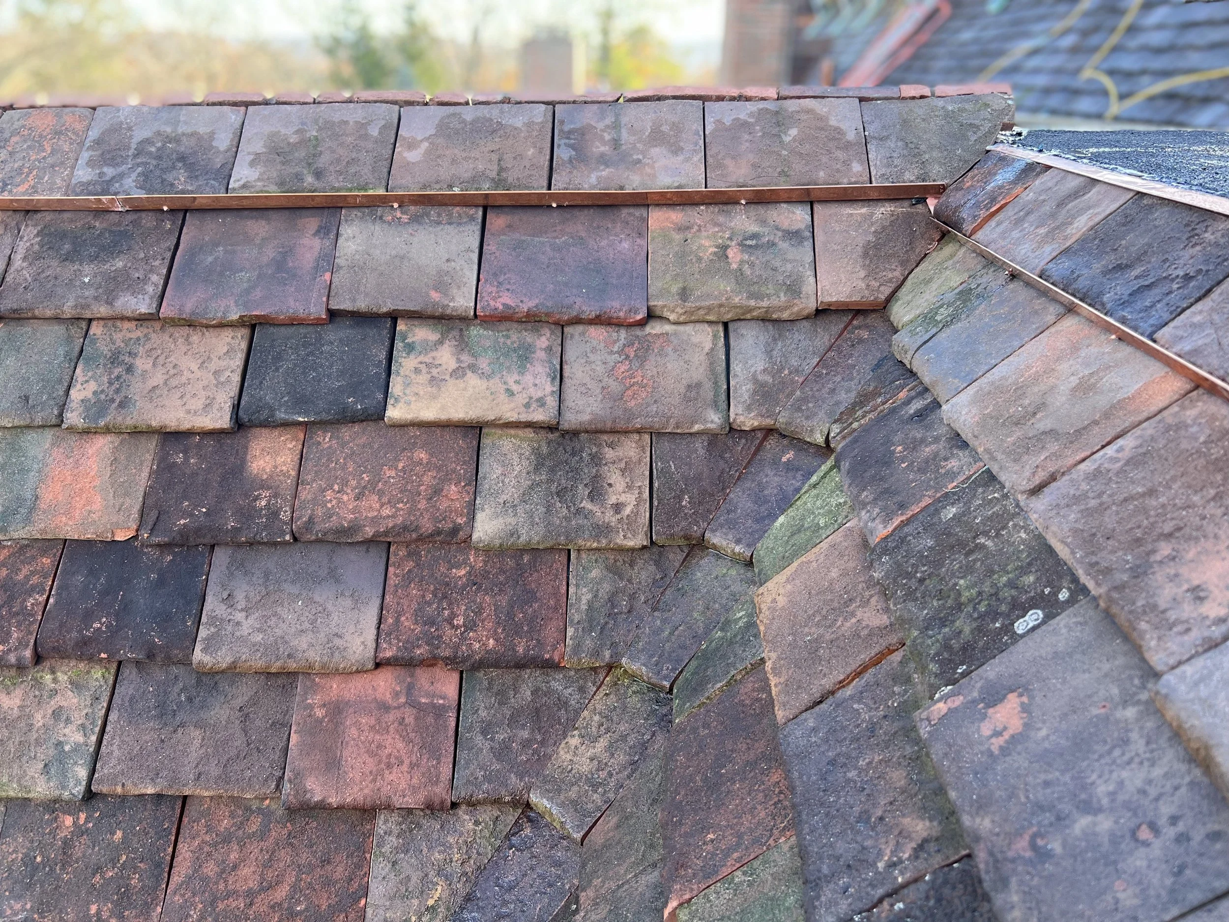 Close-up of a section of a weathered slate roof with overlapping dark gray and reddish-brown tiles.