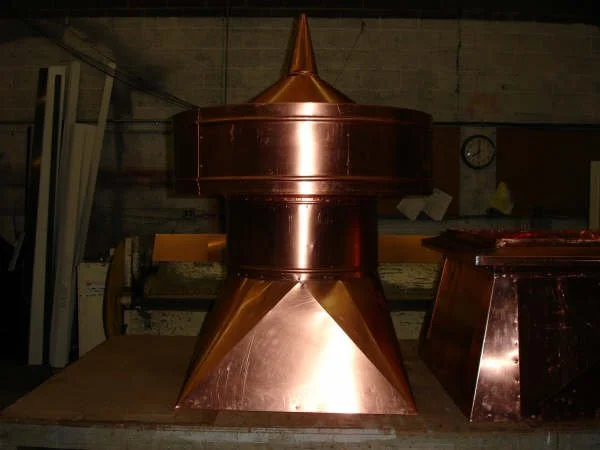A metal furnace or kiln with a pointed top, placed on a wooden table in a workshop.