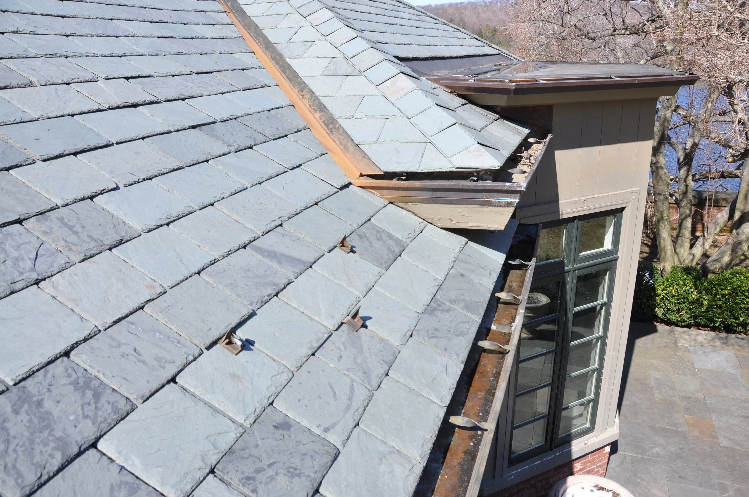 A residential house roof with slate shingles and a dormer window.