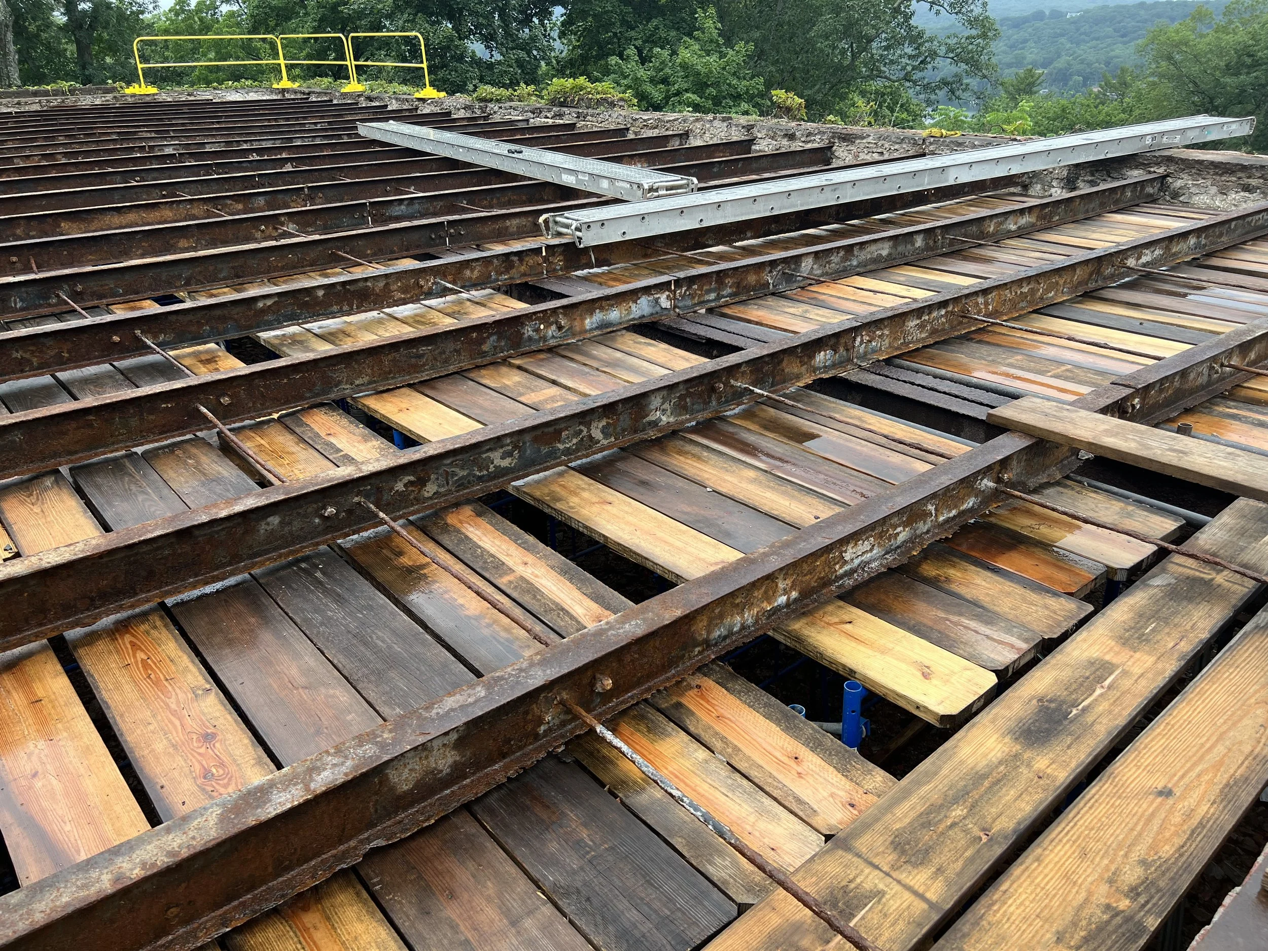 Railroad tracks with some wood planks, metal parts, and construction fixtures, surrounded by lush green trees and distant mountains.