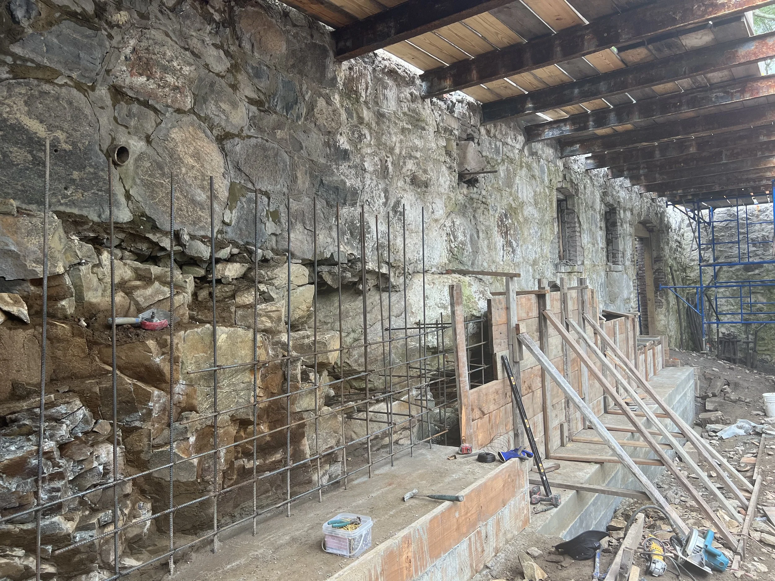 Construction work at an old stone building showing exposed stone wall and scaffolding.