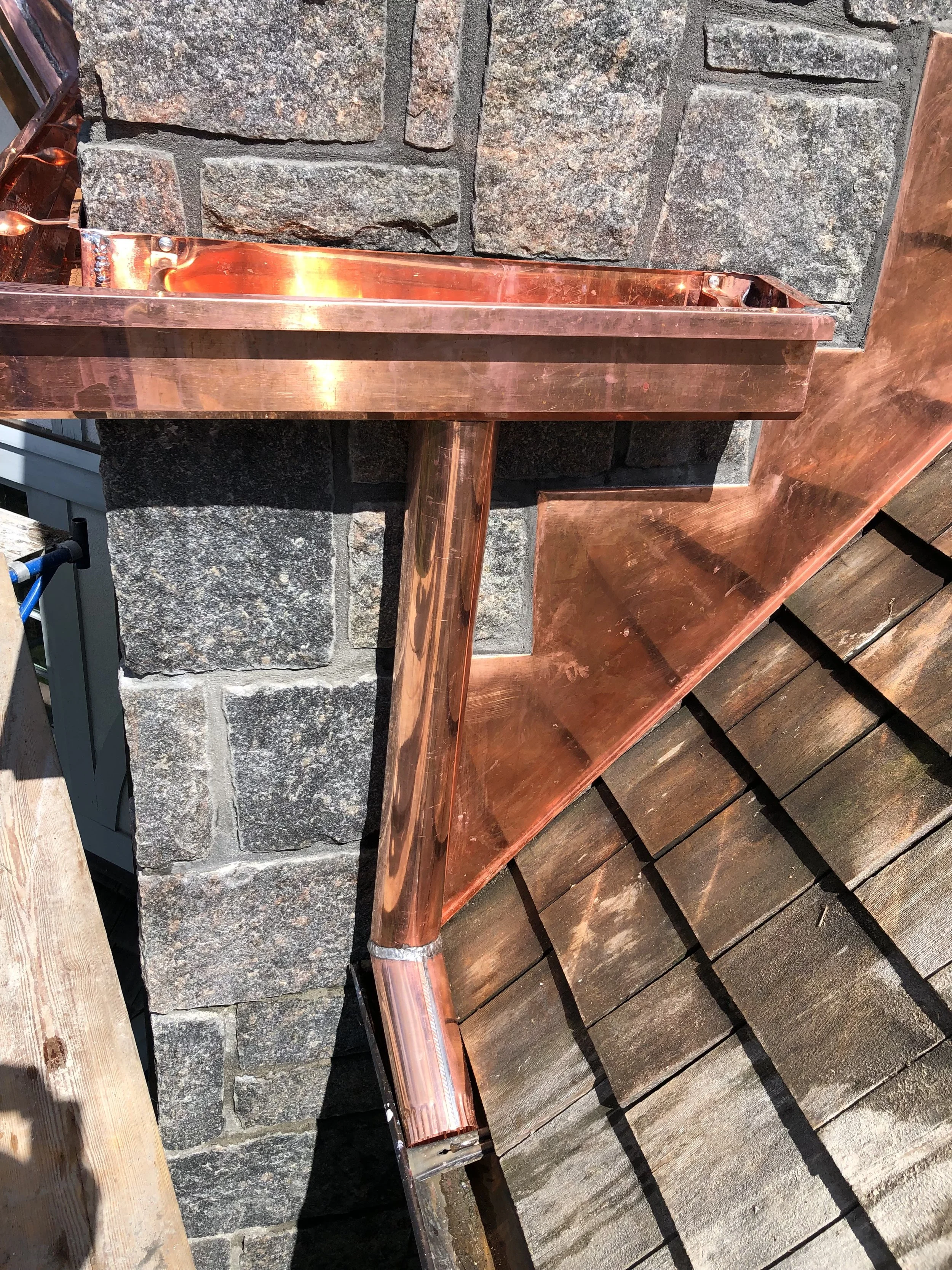 Close-up of a copper gutter attached to a stone wall with a wooden deck below.