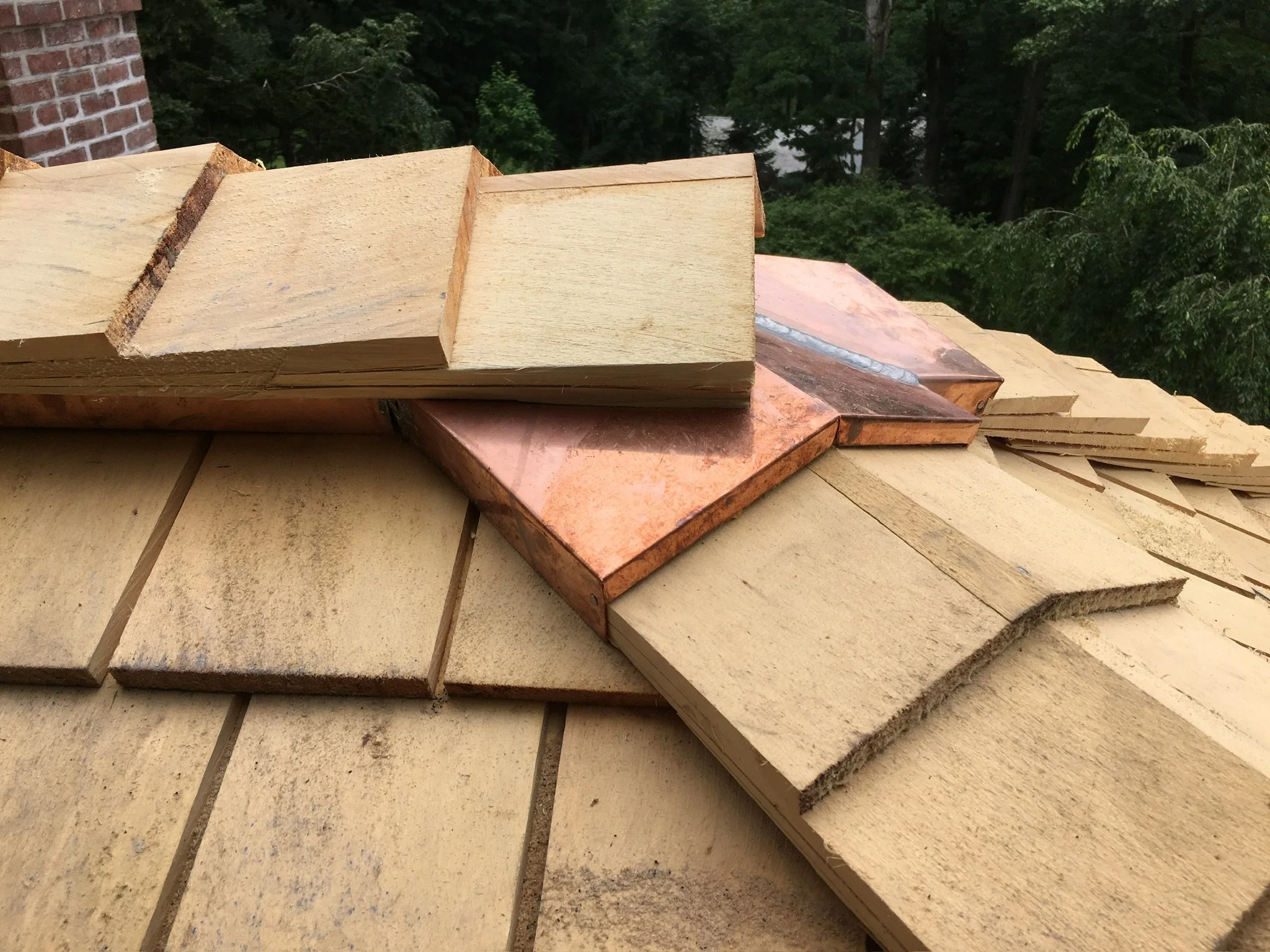 Wooden shingles or planks stacked on a roof, with trees in the background.