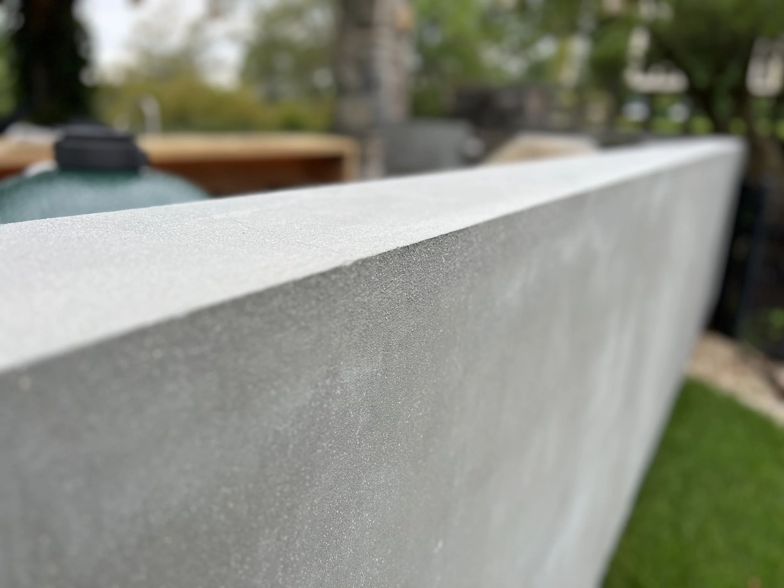 Close-up of a gray concrete or stone ledge or wall with a blurred background of trees and greenery.