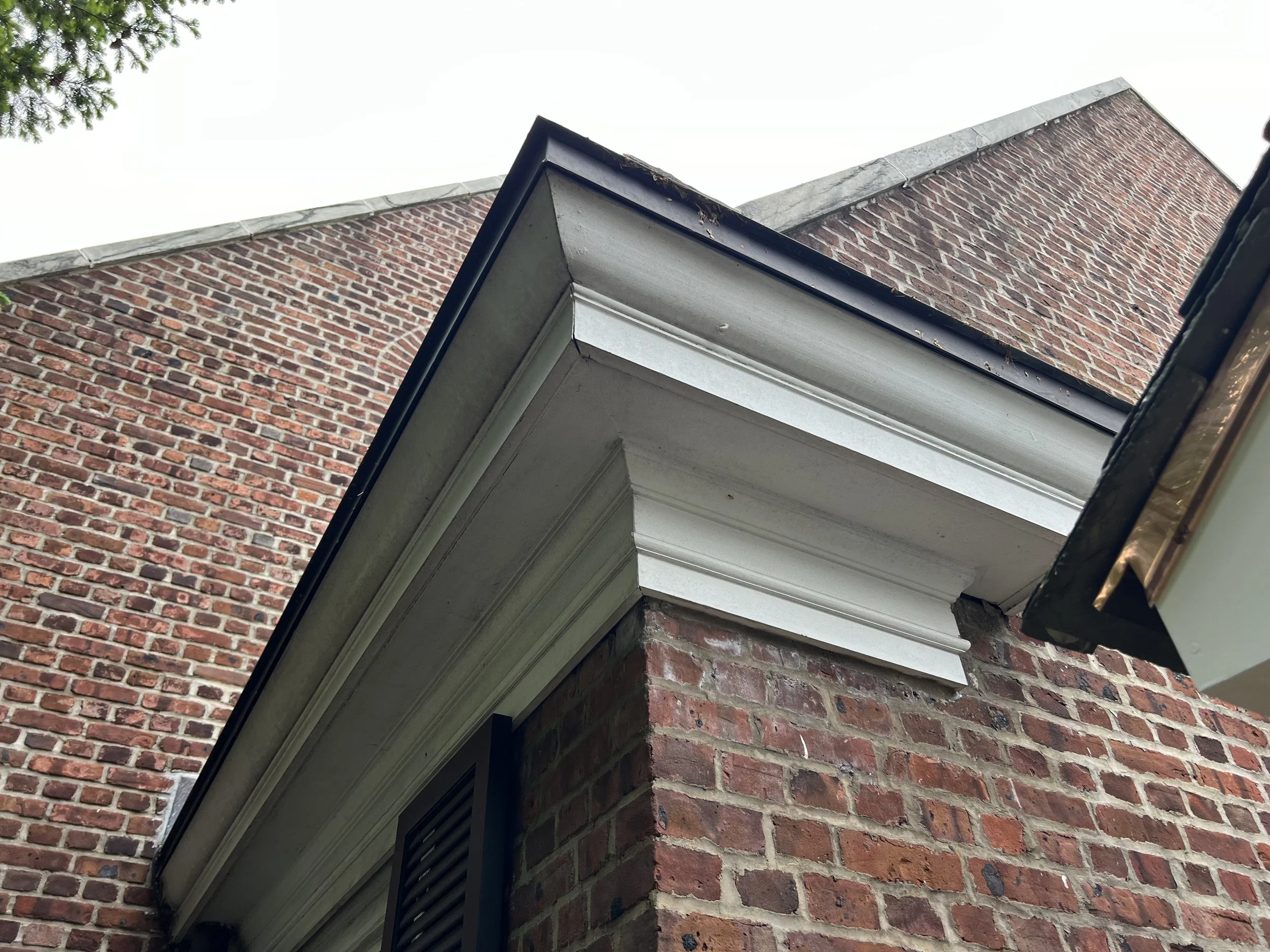 Close-up view of the corner of a brick building with a roof overhang, showing the red brick wall and part of the roof structure.