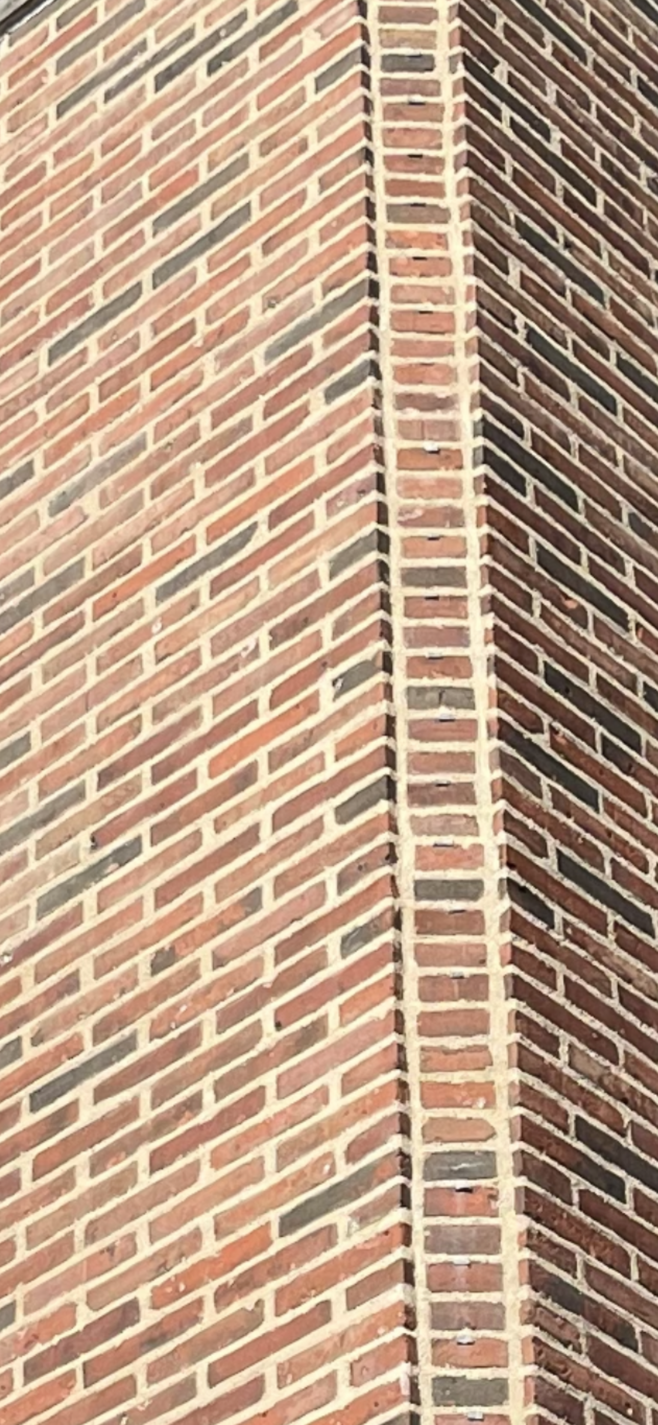 Close-up view of a brick wall with a corner formed by vertical and diagonal lines of bricks and mortar.