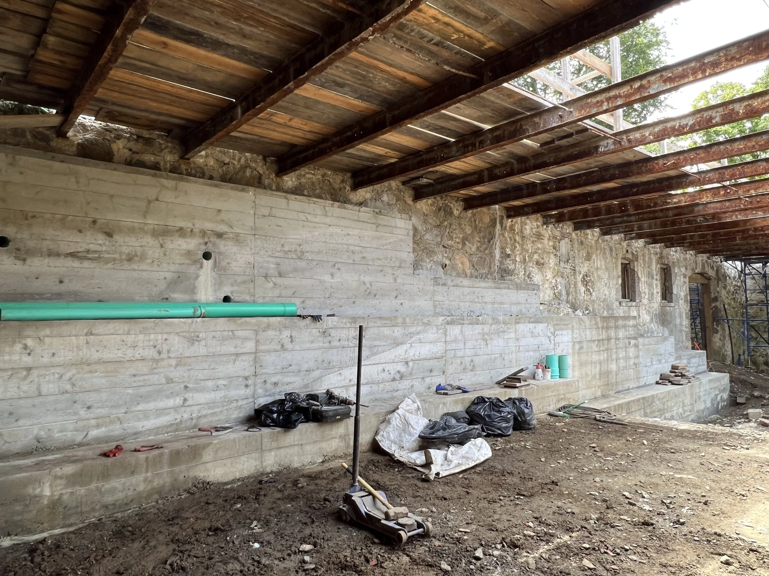 Under construction site with stone and concrete walls and exposed wooden roof beams, construction tools and debris on the ground.