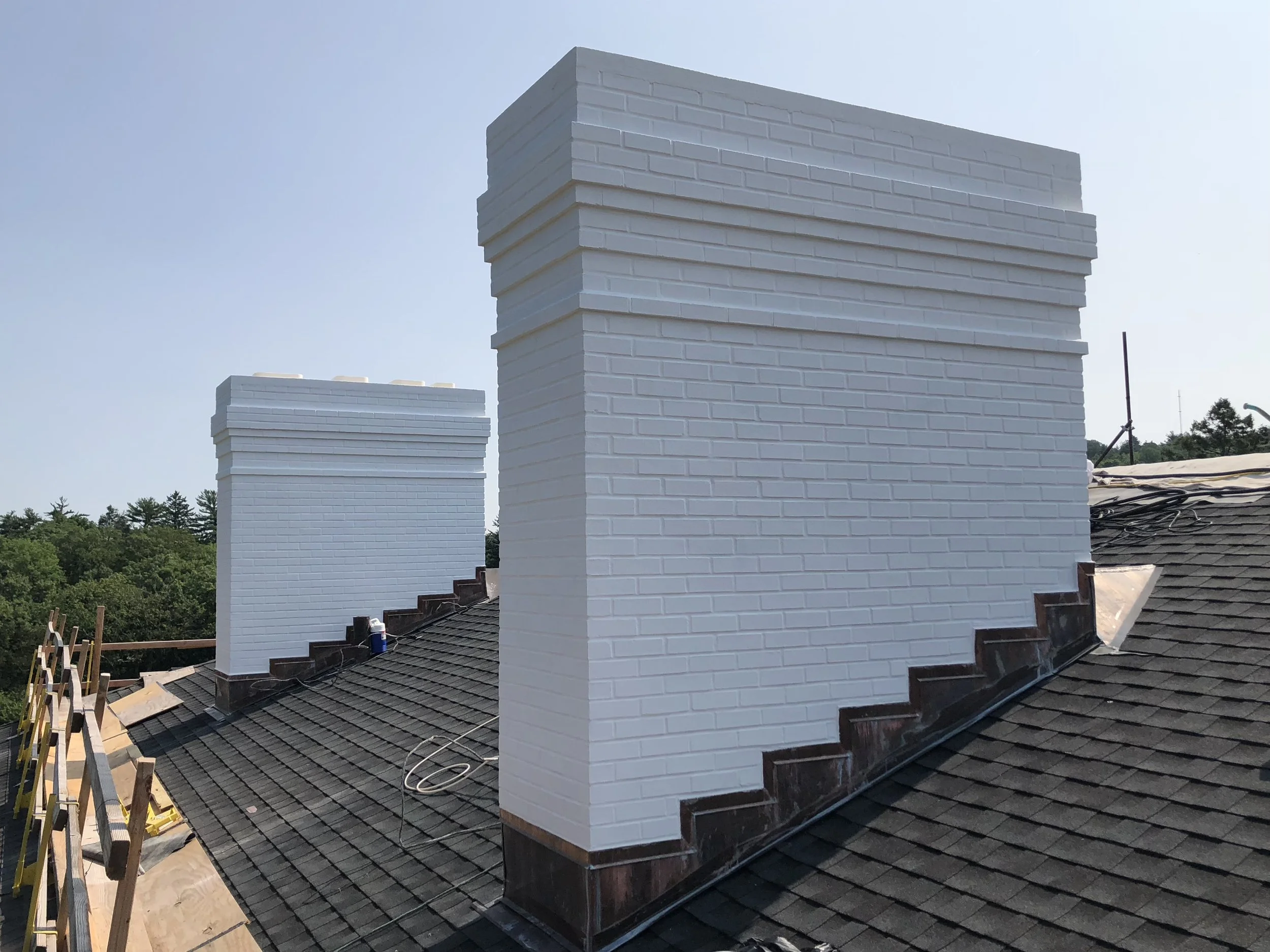White painted brick chimneys on a rooftop against a clear blue sky, with some construction materials and tools visible around.