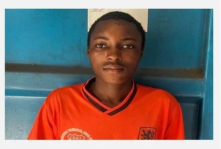 A young boy with short hair wearing an orange sports jersey, standing in front of a blue wall.