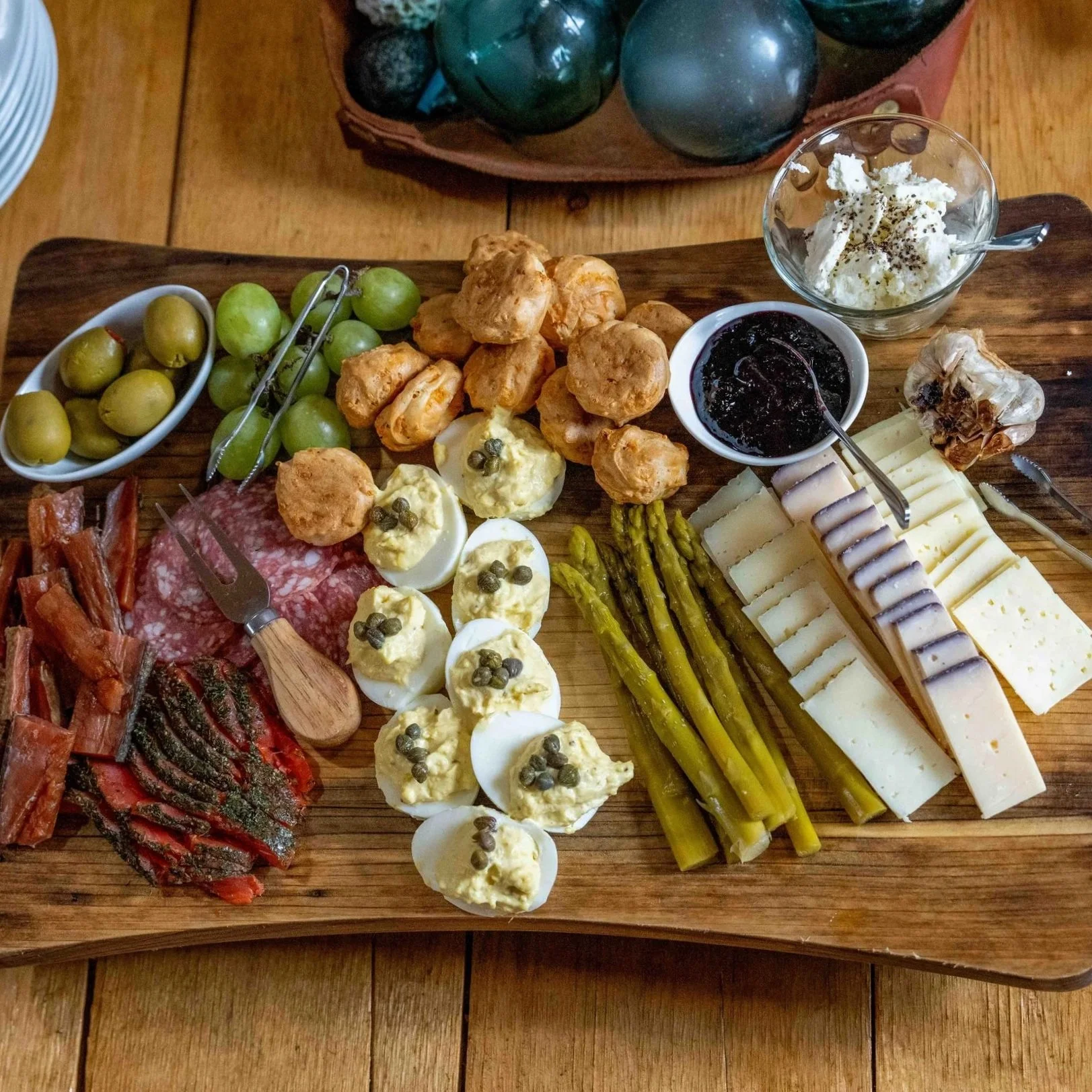 Charcuterie board with green olives, deviled eggs with capers, roasted vegetables, smoked salmon, cheese, asparagus, and dips on a wooden serving board.