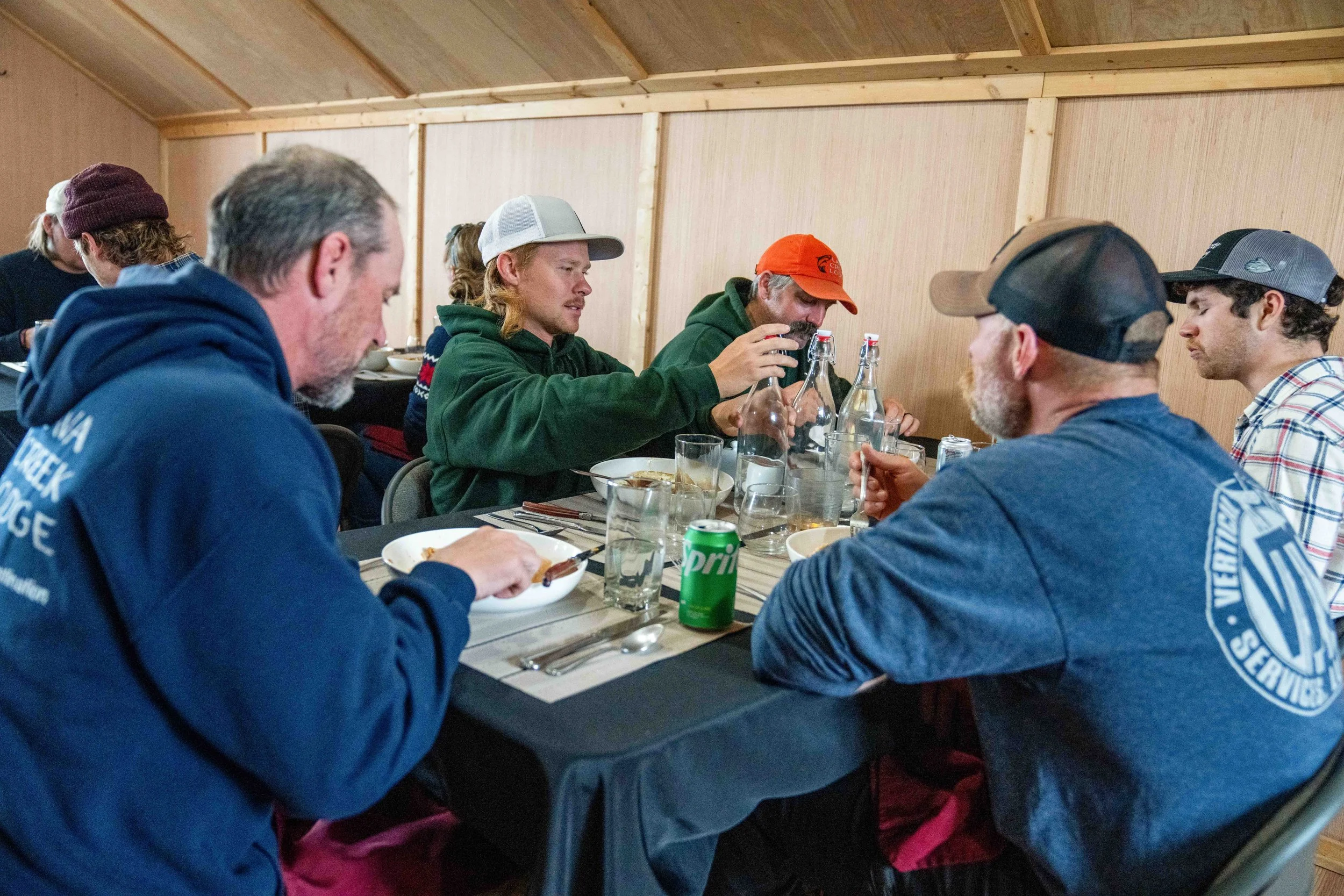 Group of people sitting at a table inside a wood-paneled room, eating and drinking.