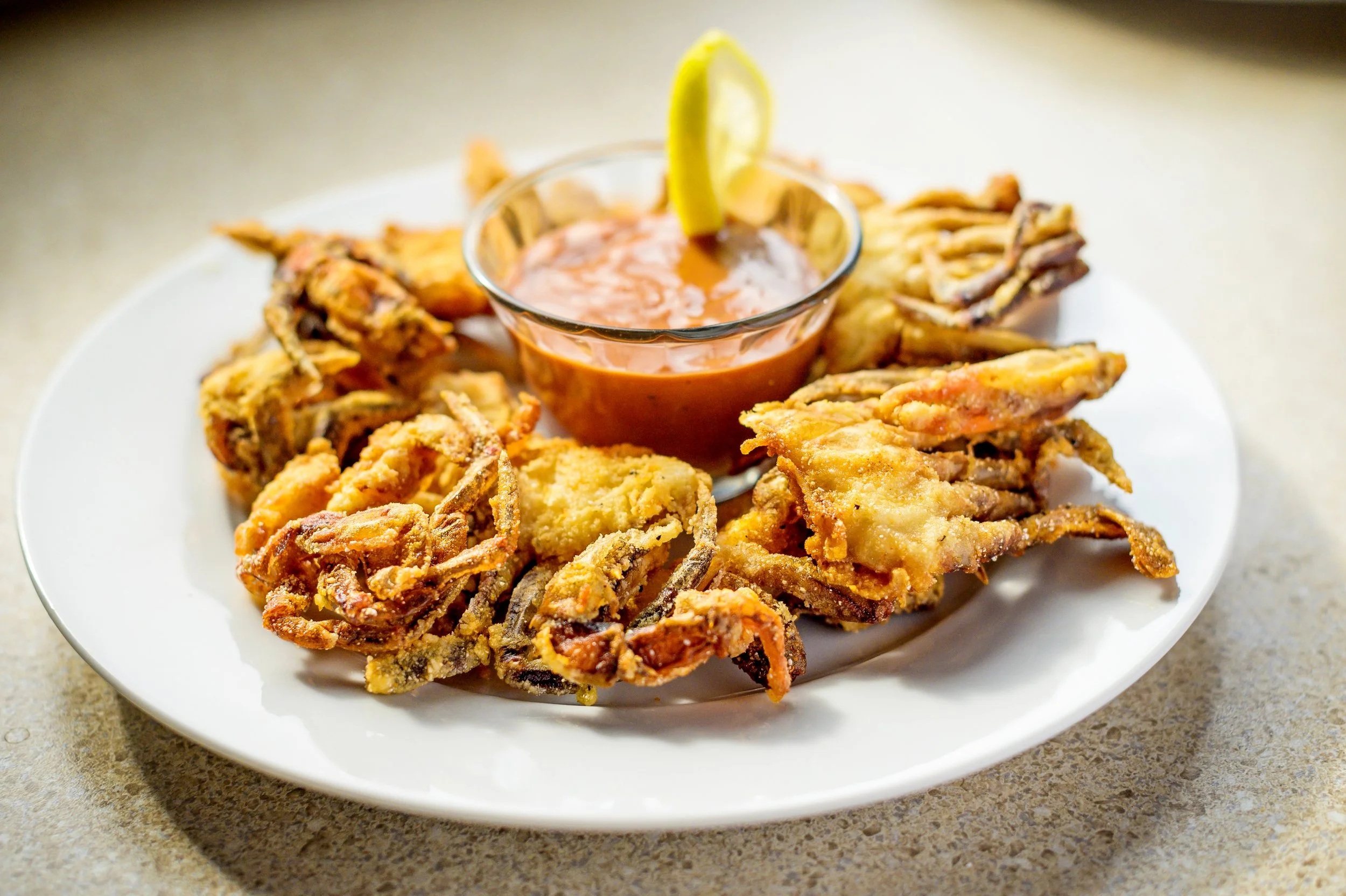 Fried fish fillets arranged on a white plate with a small bowl of dipping sauce garnished with a lemon wedge.