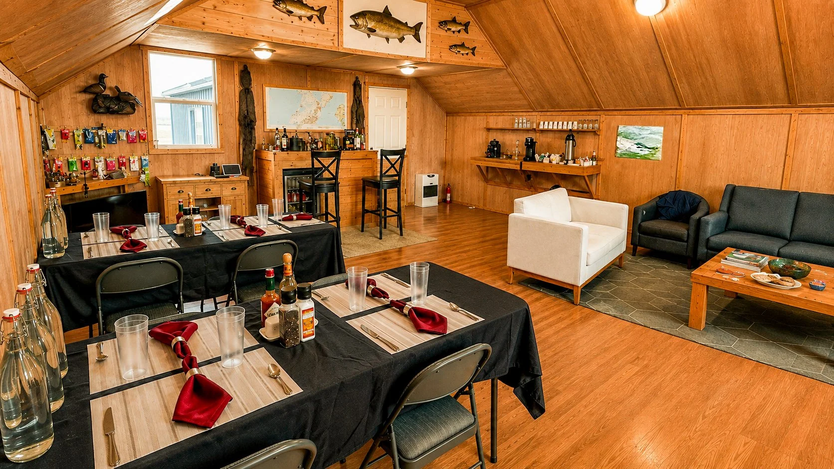 A cozy cabin-style dining area with a wooden interior, a table set for a meal, a bar area with barstools, and a seating lounge with sofas and a coffee table.
