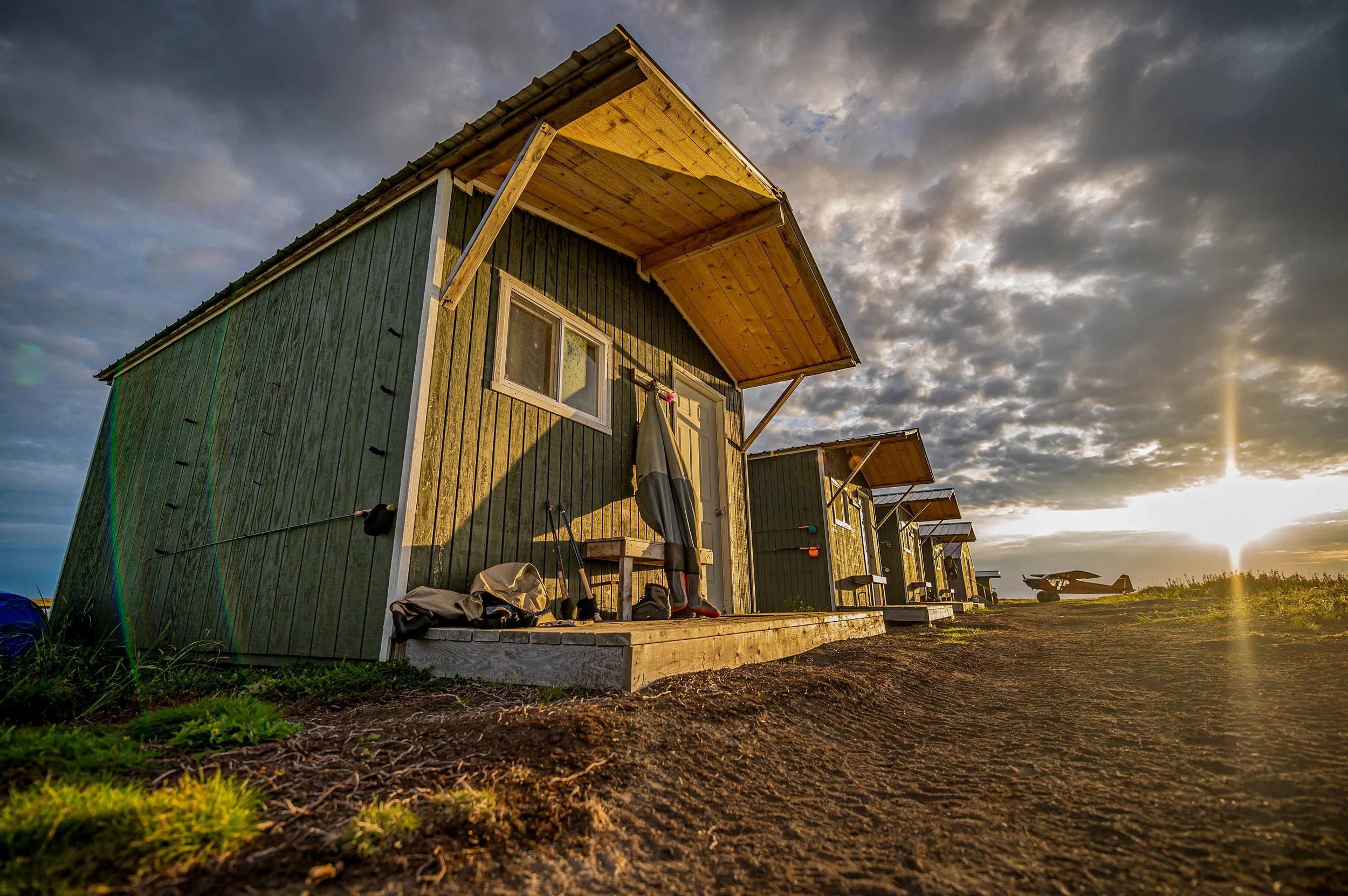 Row of guest cabins at Lava Creek Lodge at sunset, with a floatplane in the background.