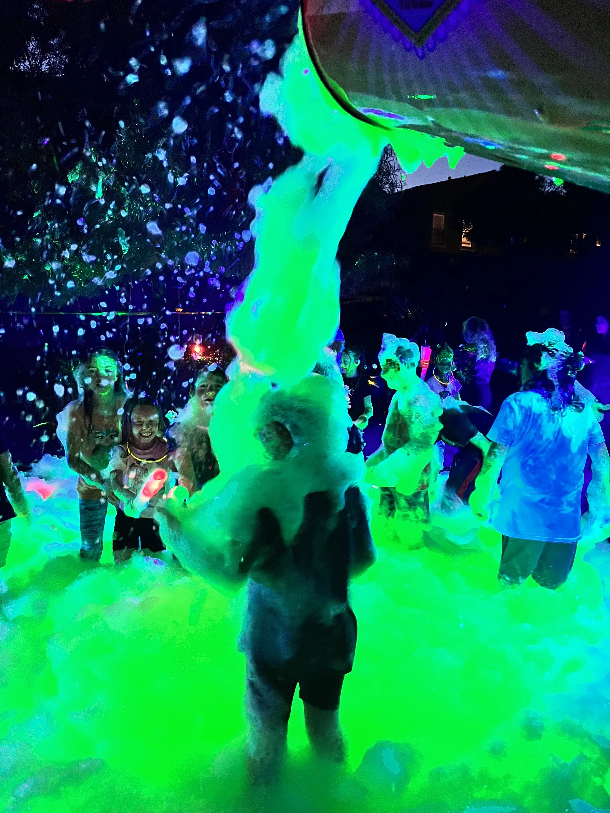 People enjoying a glow-in-the-dark water park with neon lights illuminating water and glowing waterfalls at night.