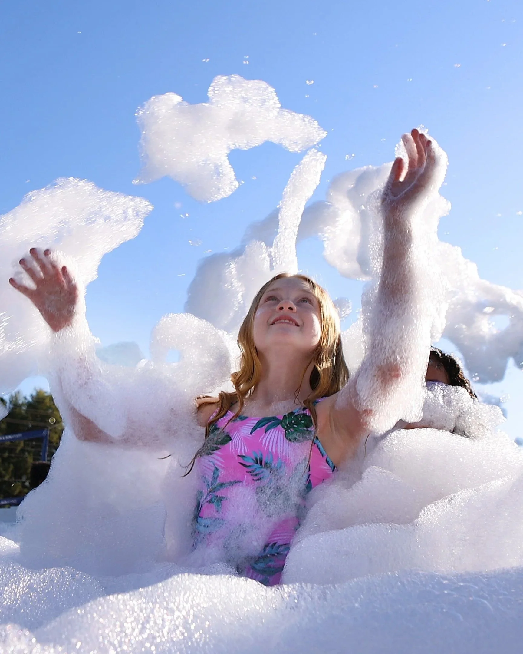 a smiling child with long hair tossing foam into the air