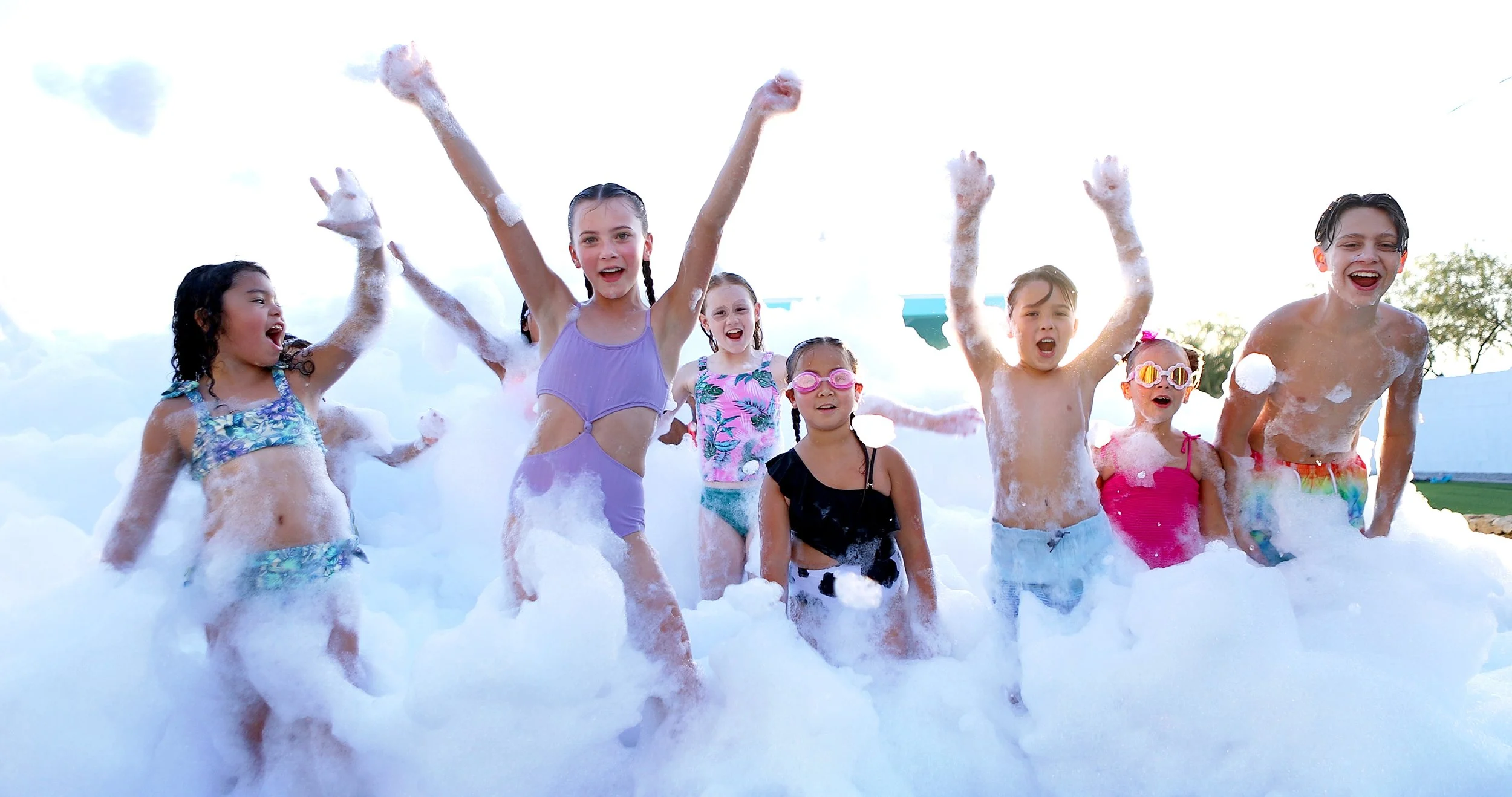a group of children in a cloud of foam with arms raised, cheering