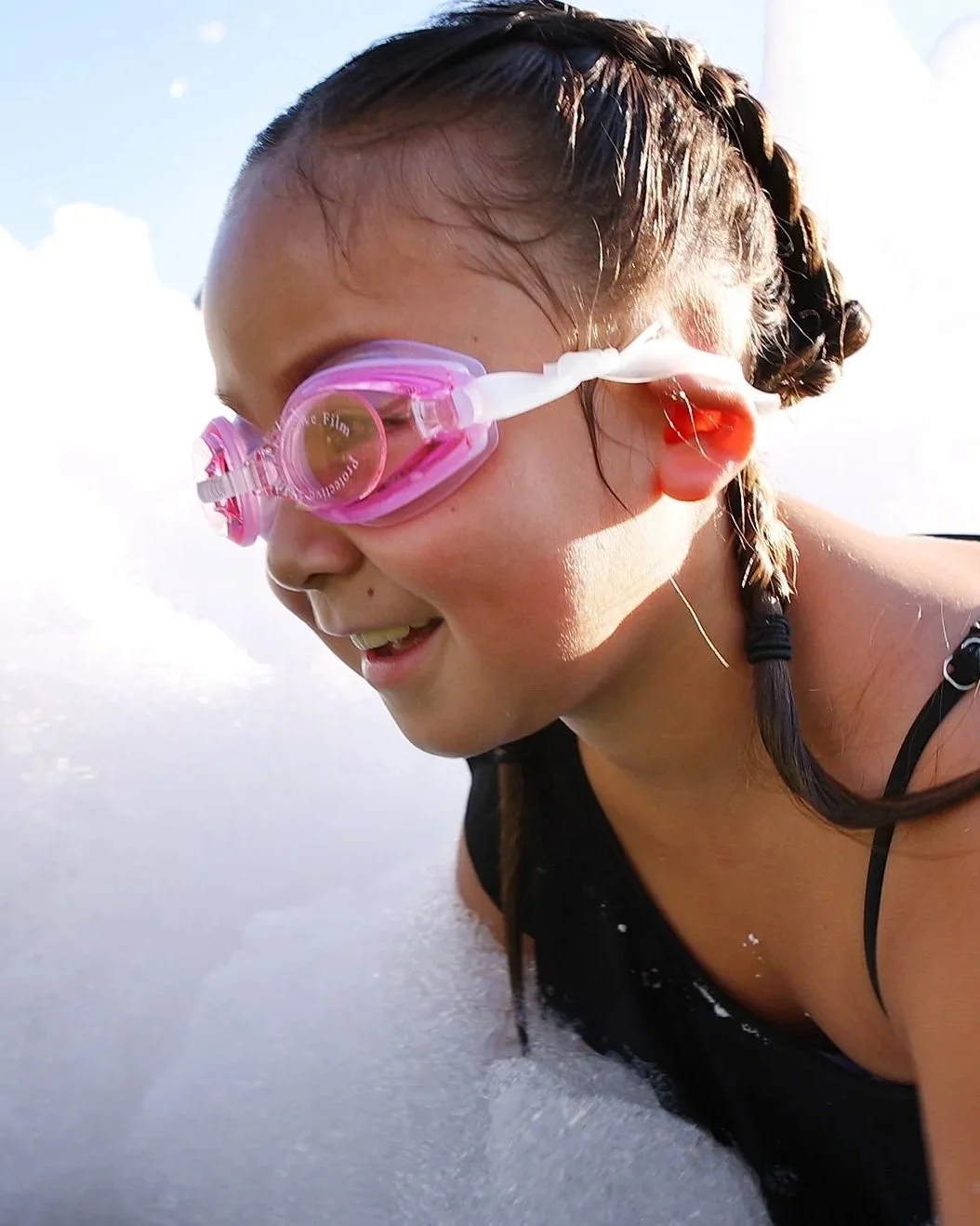 girl with goggles smiling while wading through fluffy white foam