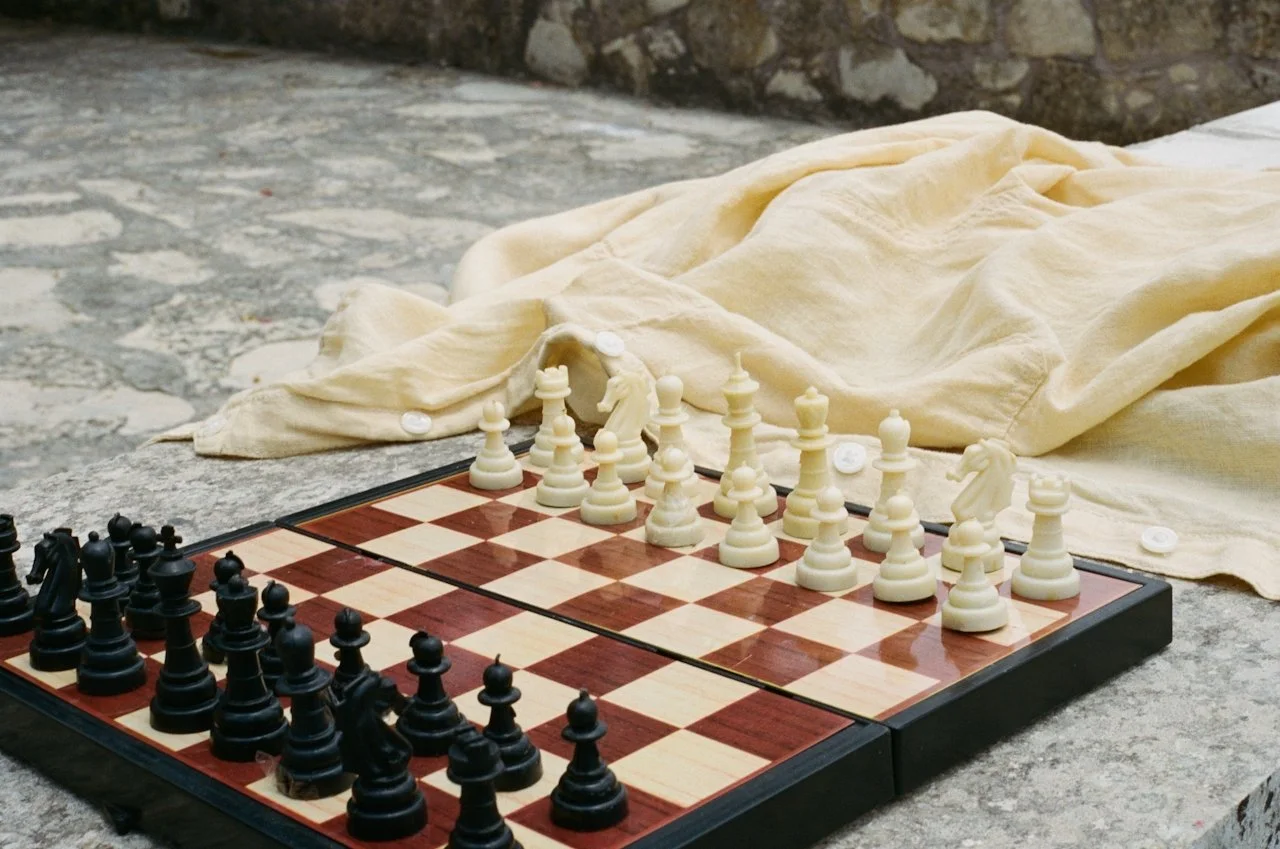 A chessboard set up with black and white pieces on a stone surface, with a beige cloth draped over part of the board.