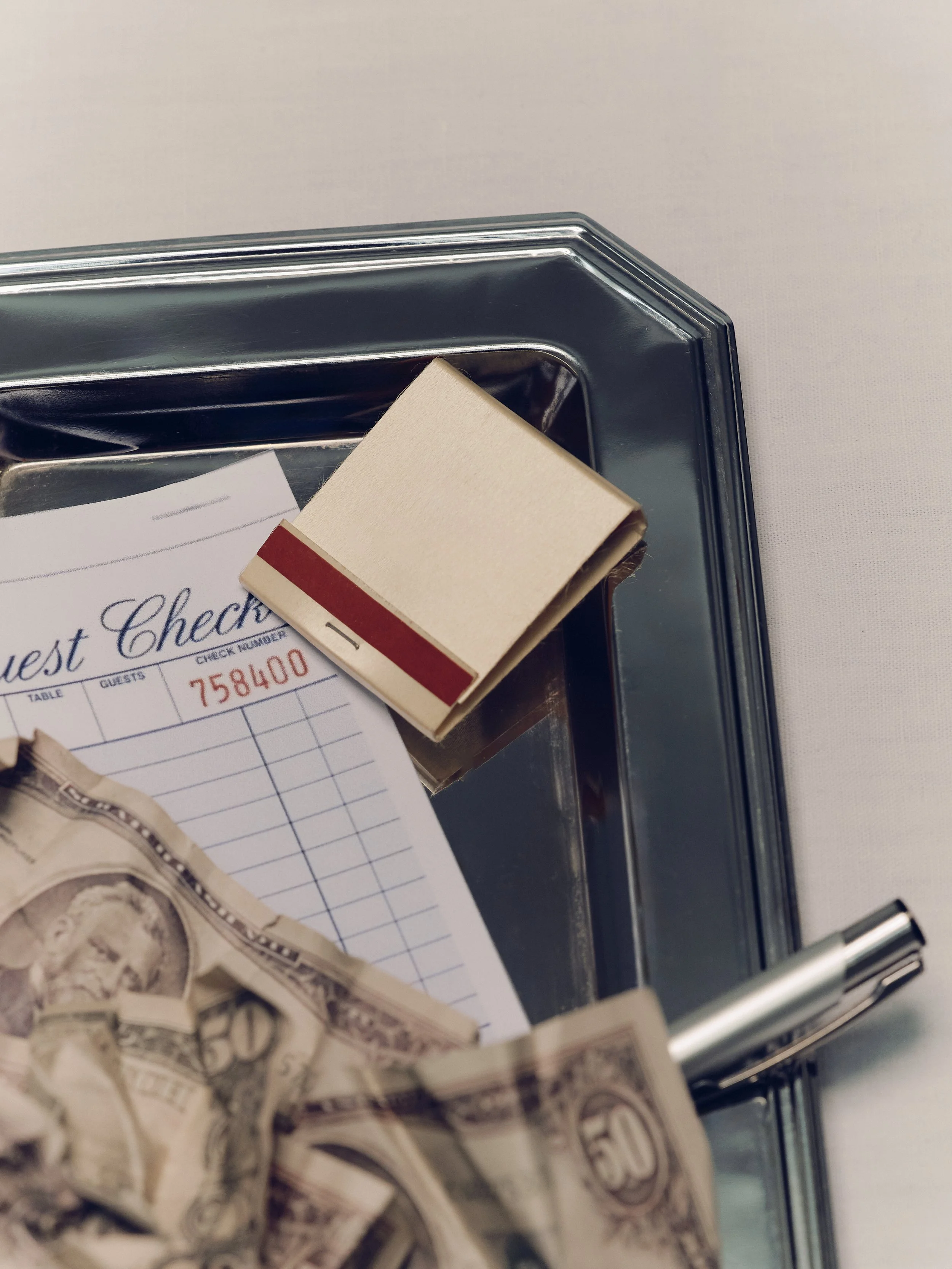 Close-up of cash bills and a receipt inside a metal cash box with a beige sticky note on top.