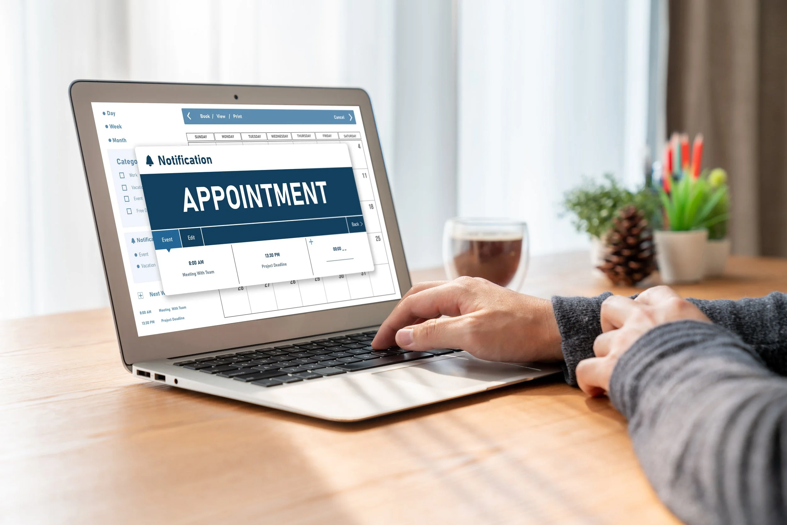 Laptop screen displaying a notification for an appointment, with a calendar and schedule details in the background, on a wooden desk with a glass of coffee and plant in the background.