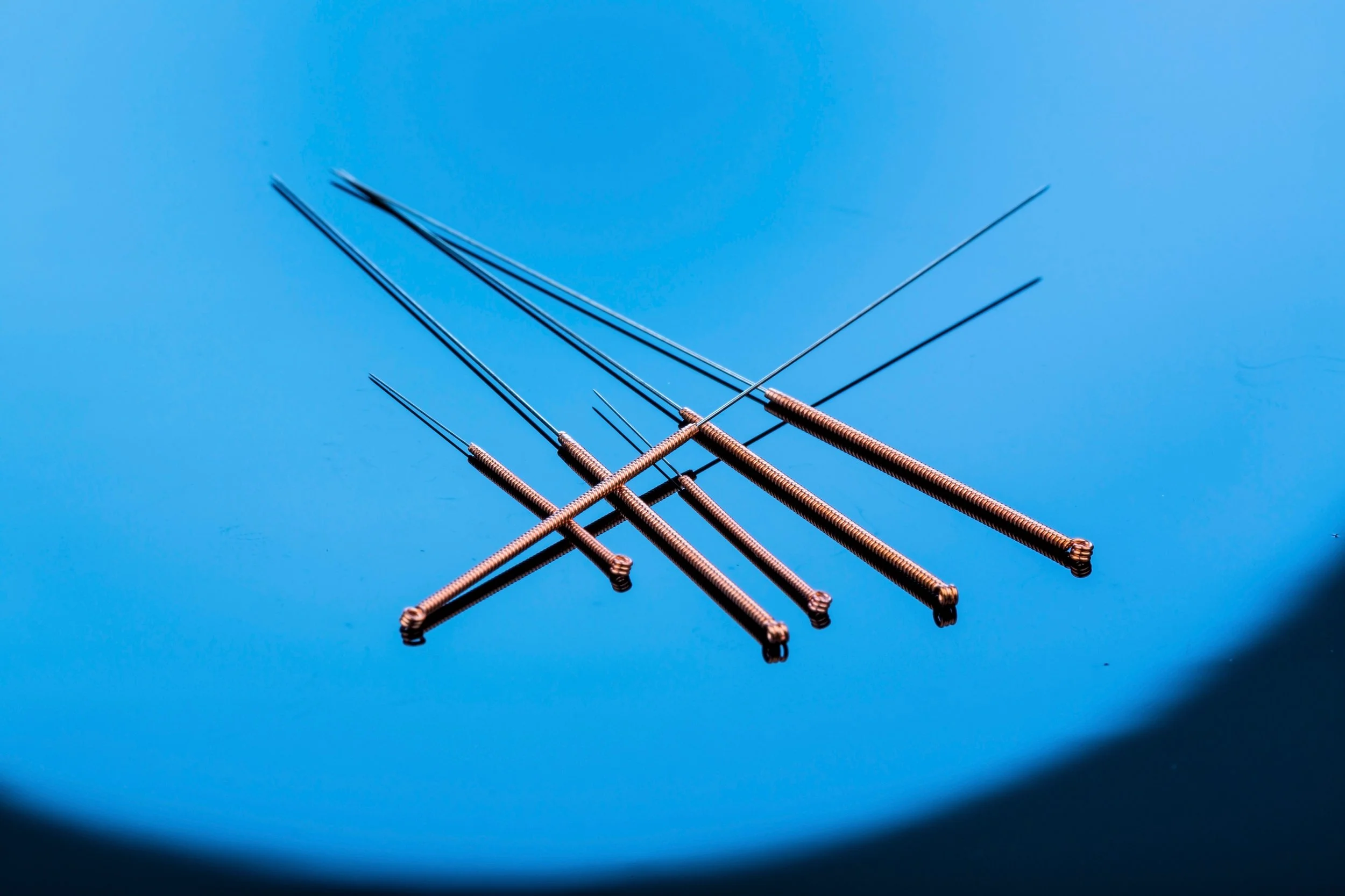 Multiple heated metal needles arranged in a fan pattern on a bright blue background.
