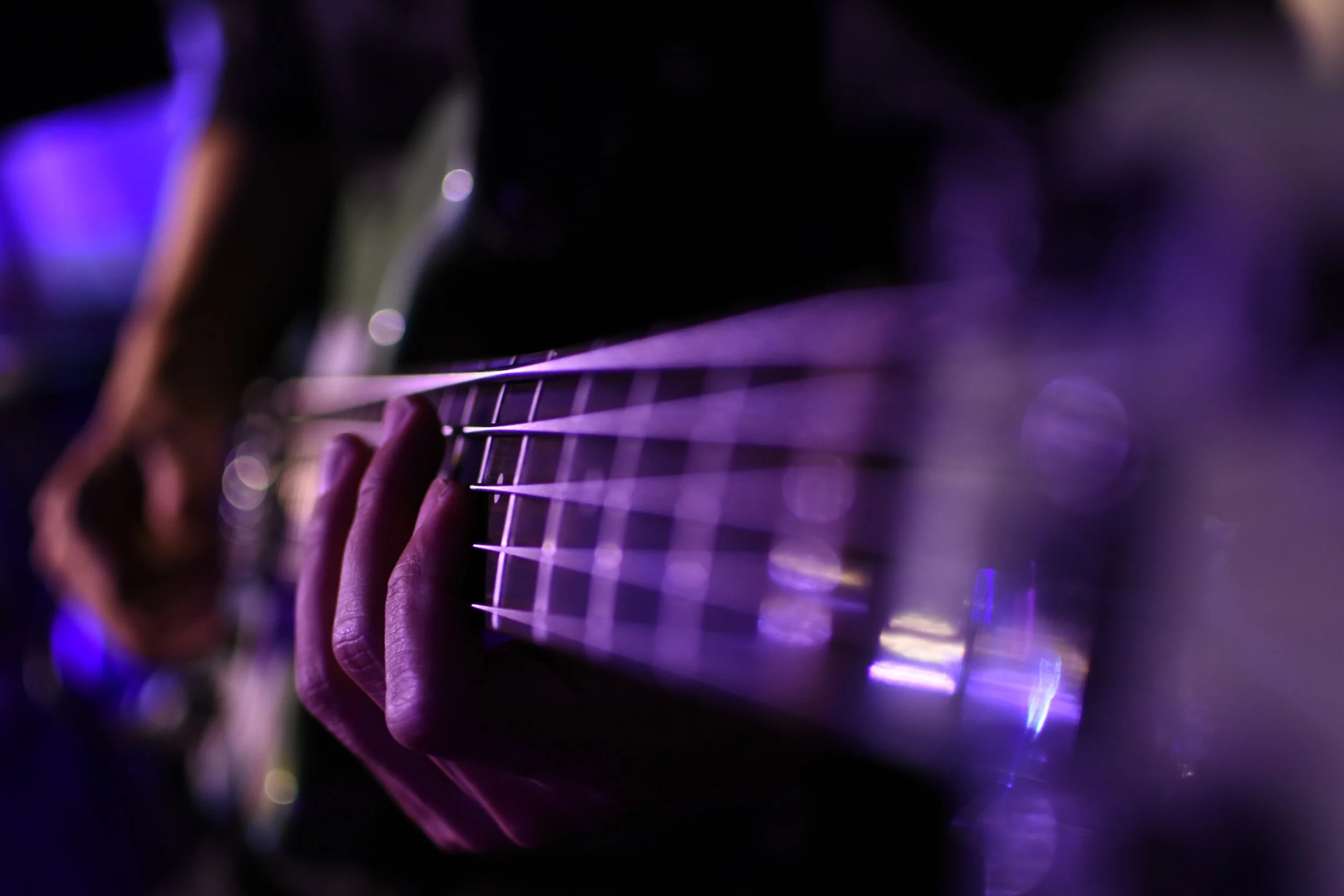 A close-up of a person playing an electric guitar with purple and blue lighting effects.