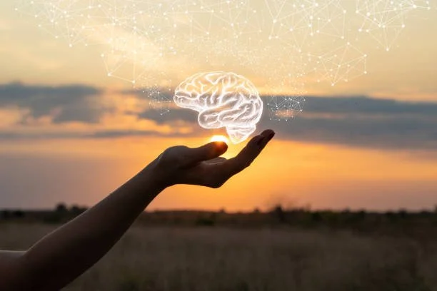 A hand holding a glowing, digital brain illustration against a sunset sky with abstract digital network graphics.