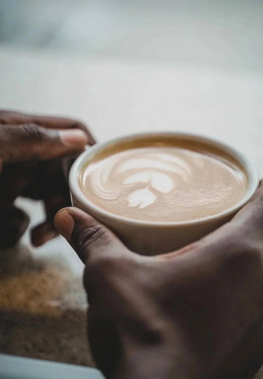 Close-up of a person holding a cup of coffee with latte art on top.