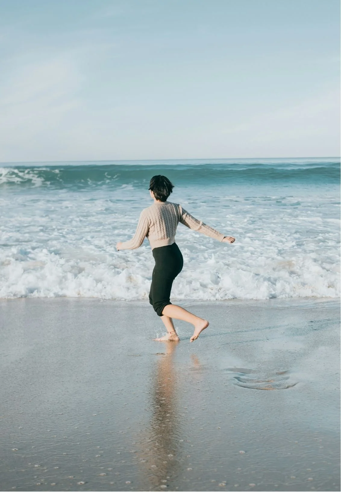 Person running along the shoreline at the beach, waves in the background under a clear sky.