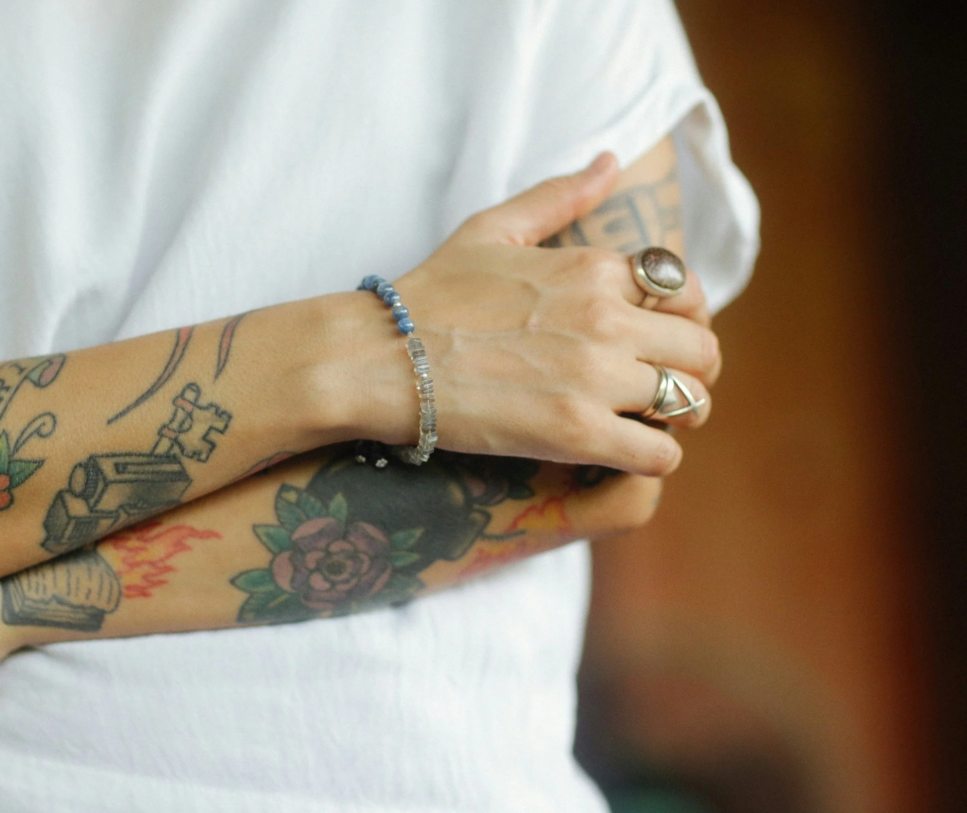 A person with tattoos on their arm is holding their chest. The person is wearing a ring and a bracelet.