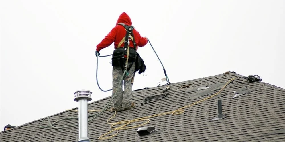 A worker in safety gear repairing a roof on a cloudy day.