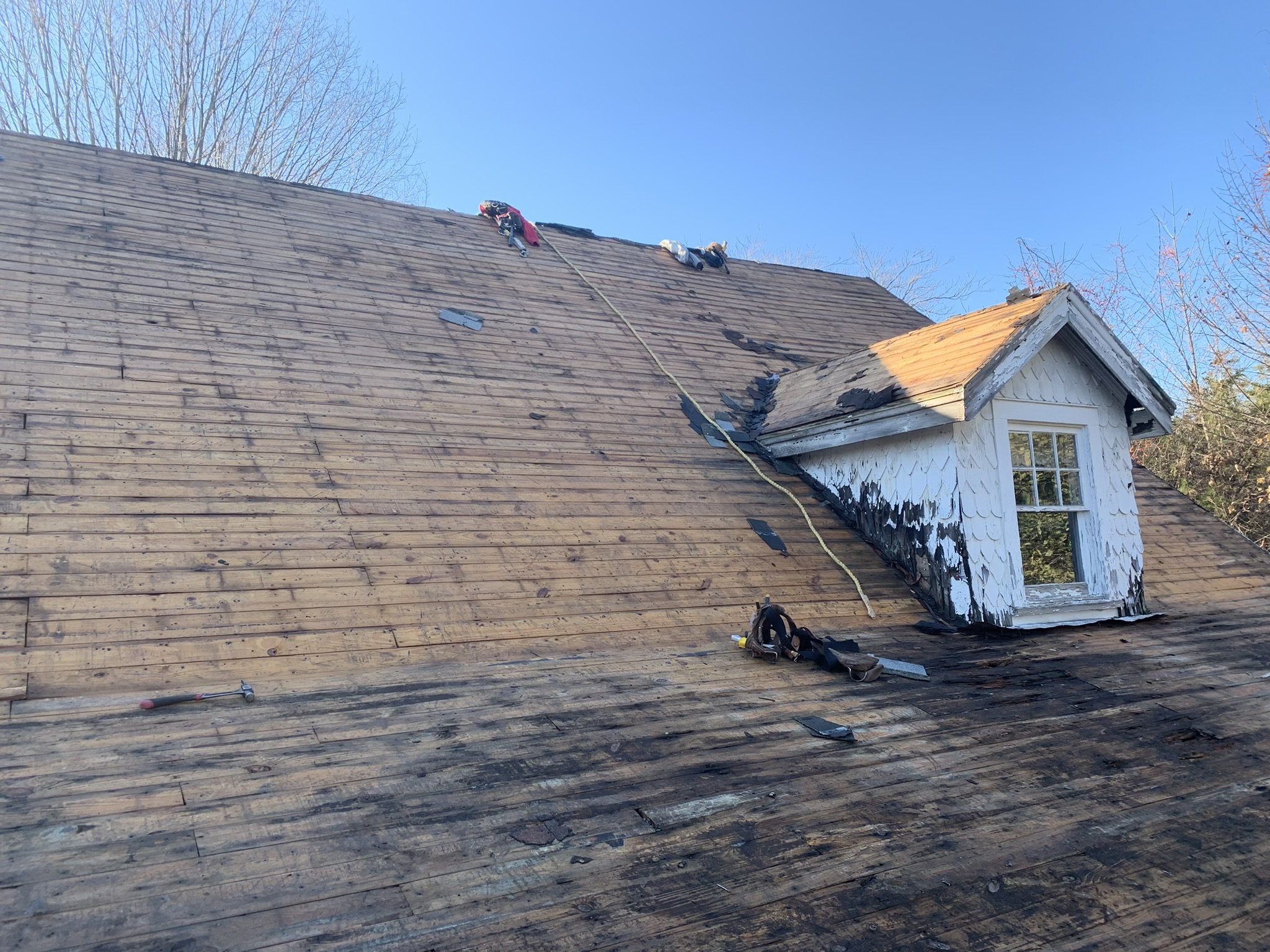 Workers replacing shingles on a house roof during daylight.
