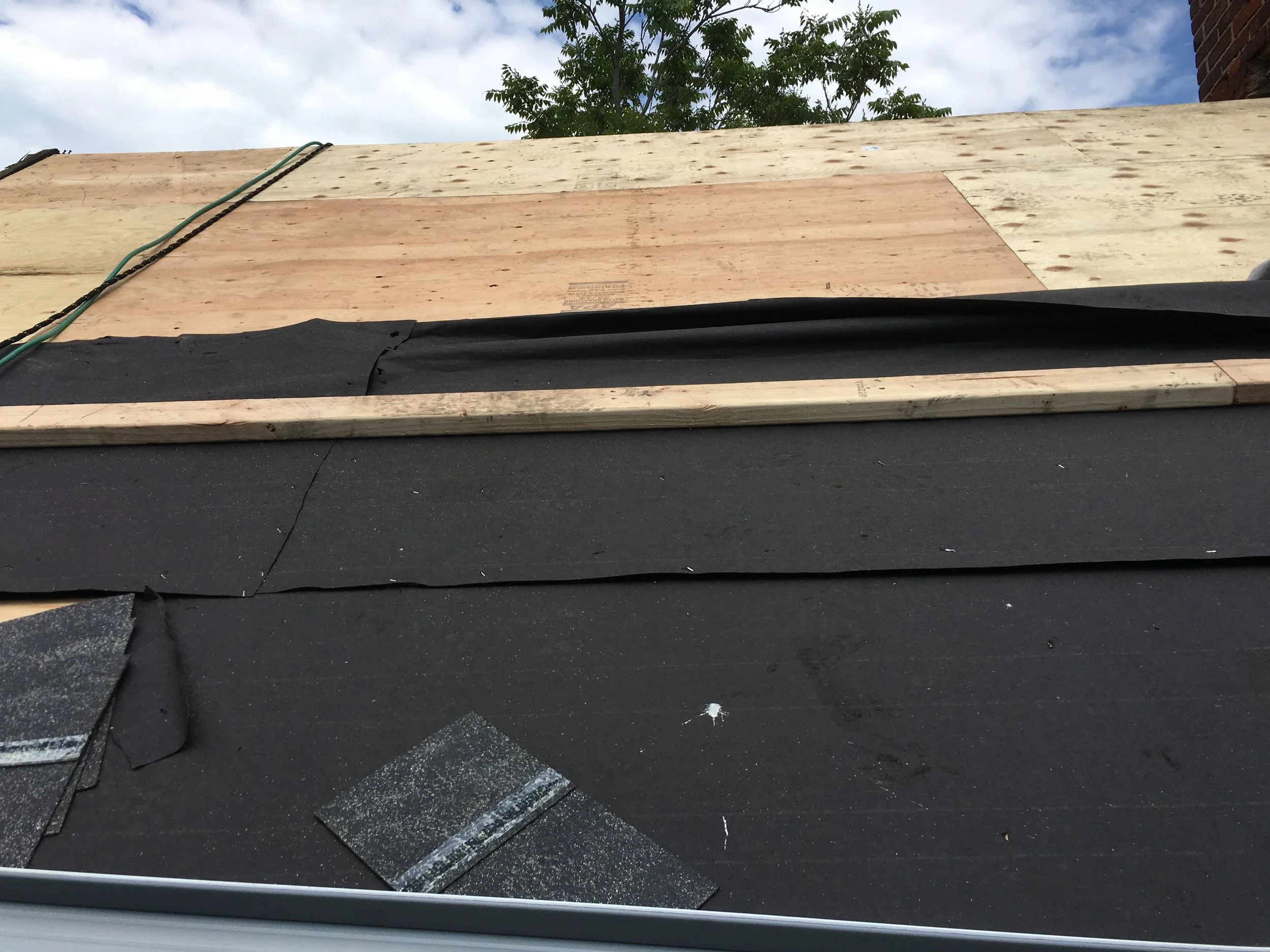 Construction site with wooden board and black roofing under blue sky with some clouds.