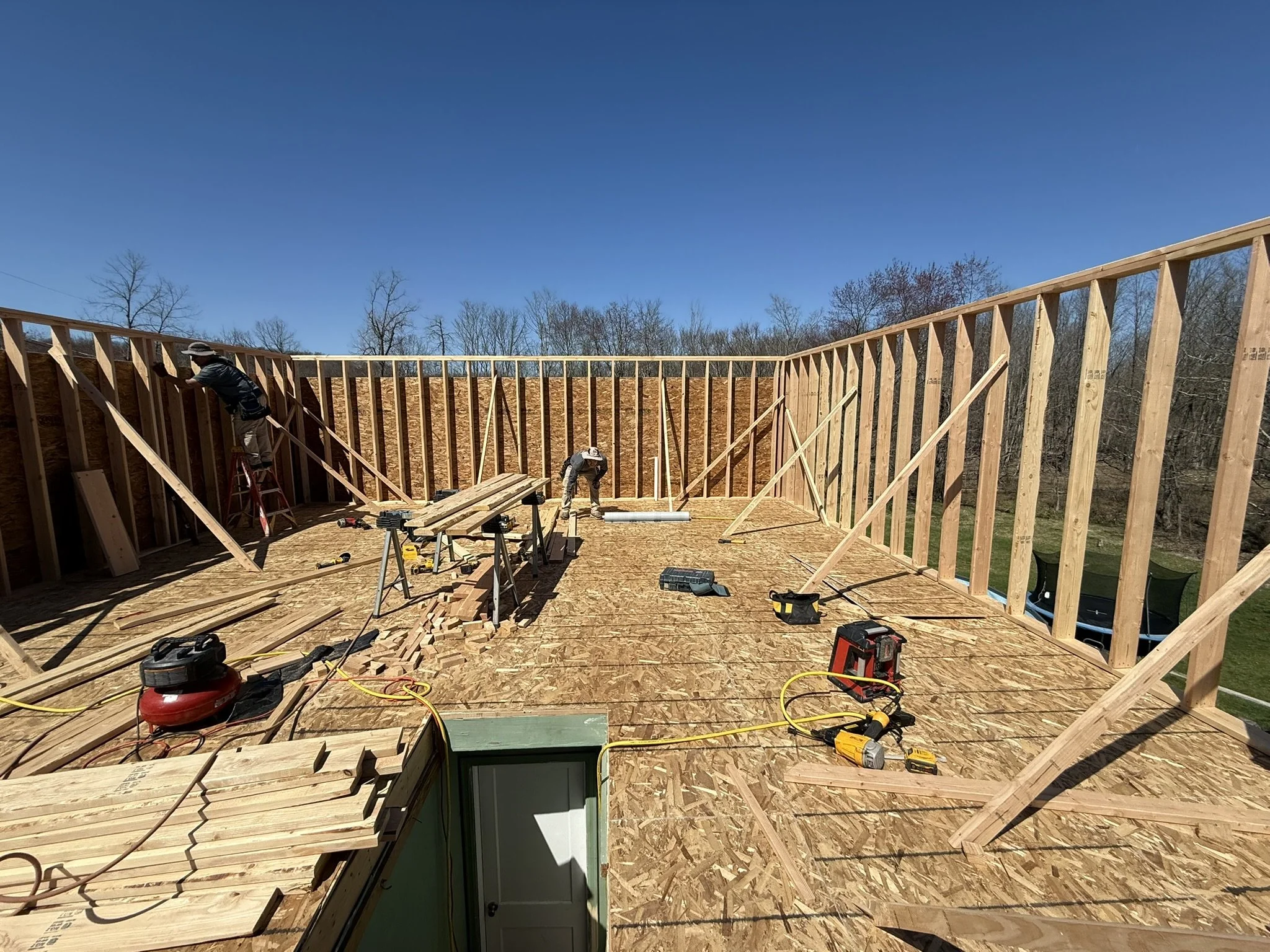Construction workers building a wooden frame for a house under a clear blue sky with leafless trees in the background.