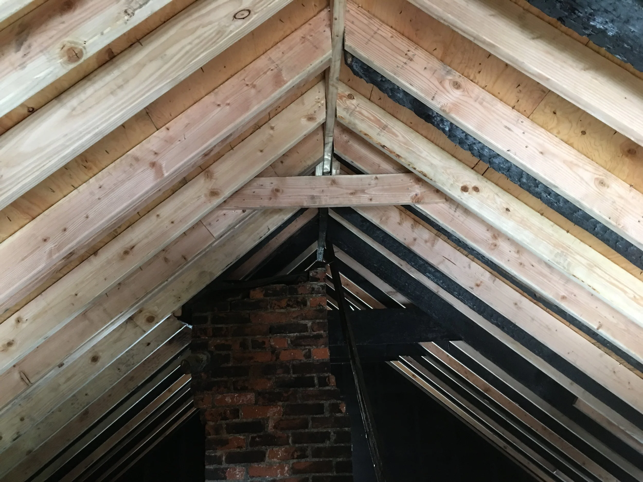 The image shows the interior of a roof with wooden rafters and a brick chimney in the center.
