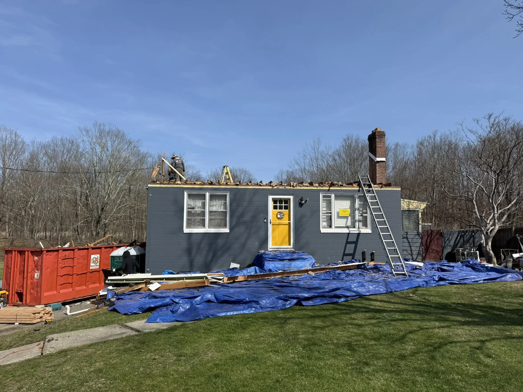 Workers replacing shingles on a house roof during daylight.