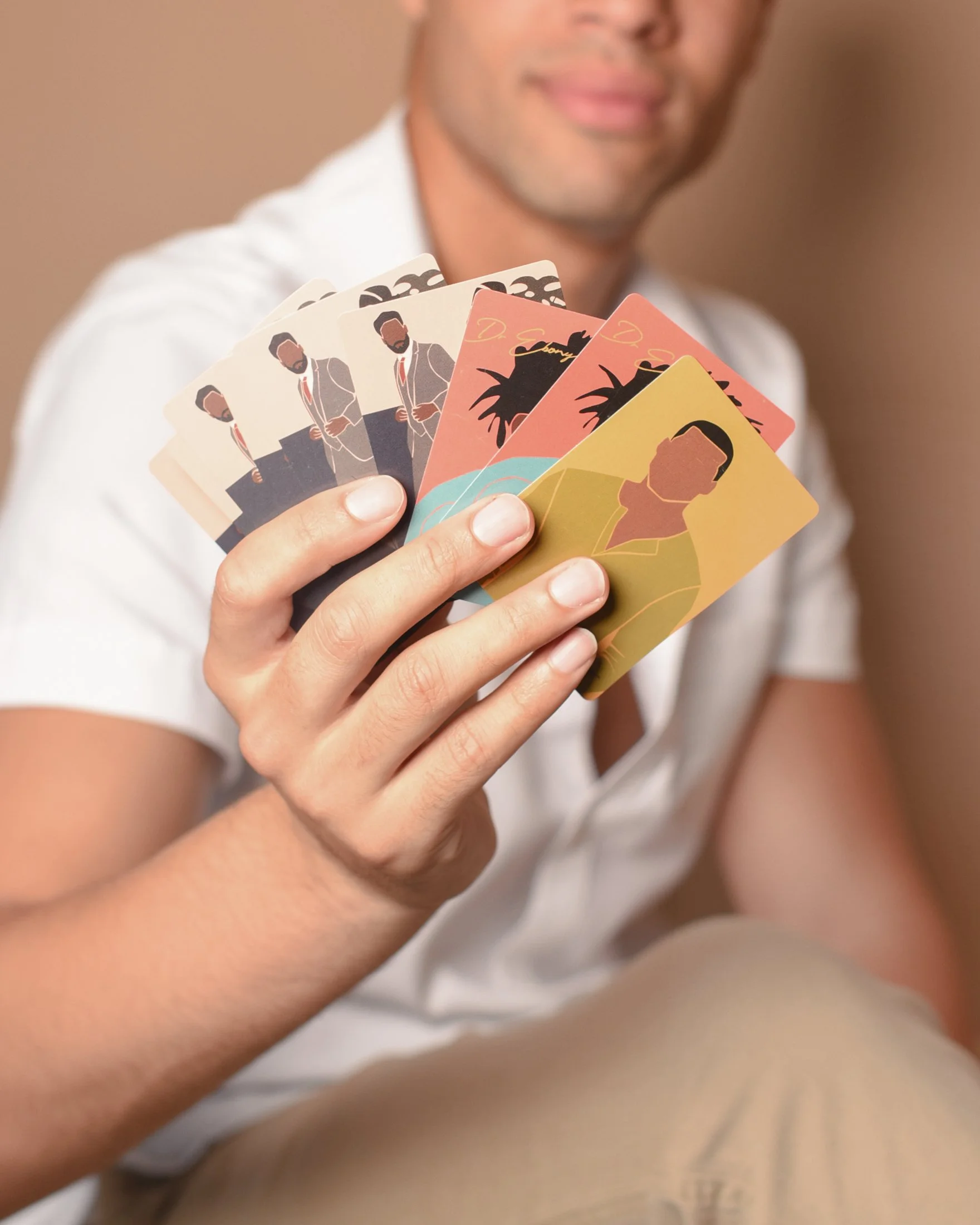 A man holding several illustrated cards in a fan shape, with blurred background.